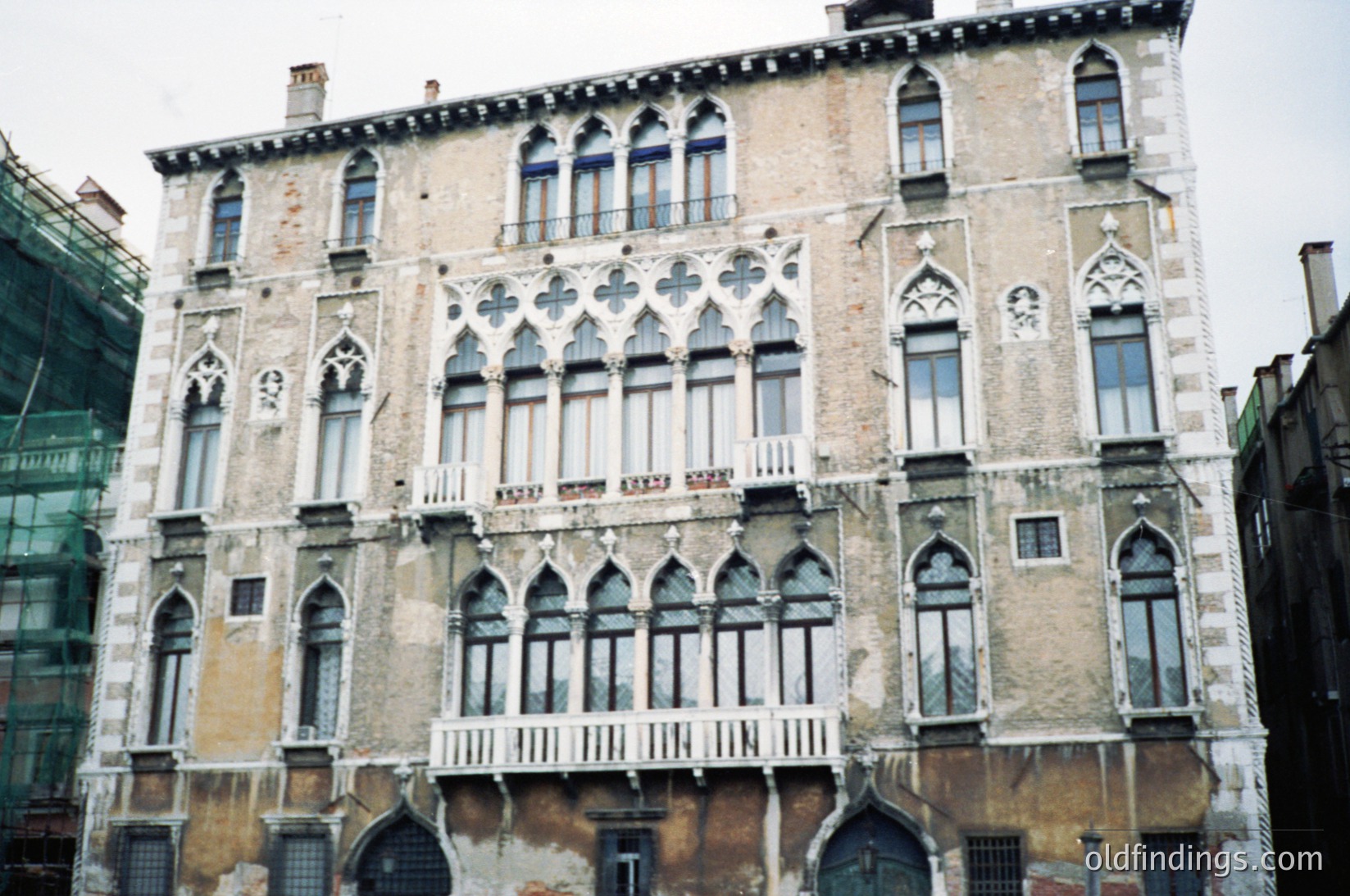 Gothic Revival façade featuring pointed arches, ornate stonework, and symmetrical windows. Three-story building with weathered plaster and exposed brick accents, indicative of Venetian architecture. Likely 19th-century construction ( ) --- *Note: No specific time period tag added as exact date isn’t discernible, but stylistic cues align with 19th-century Venetian revivalism.*