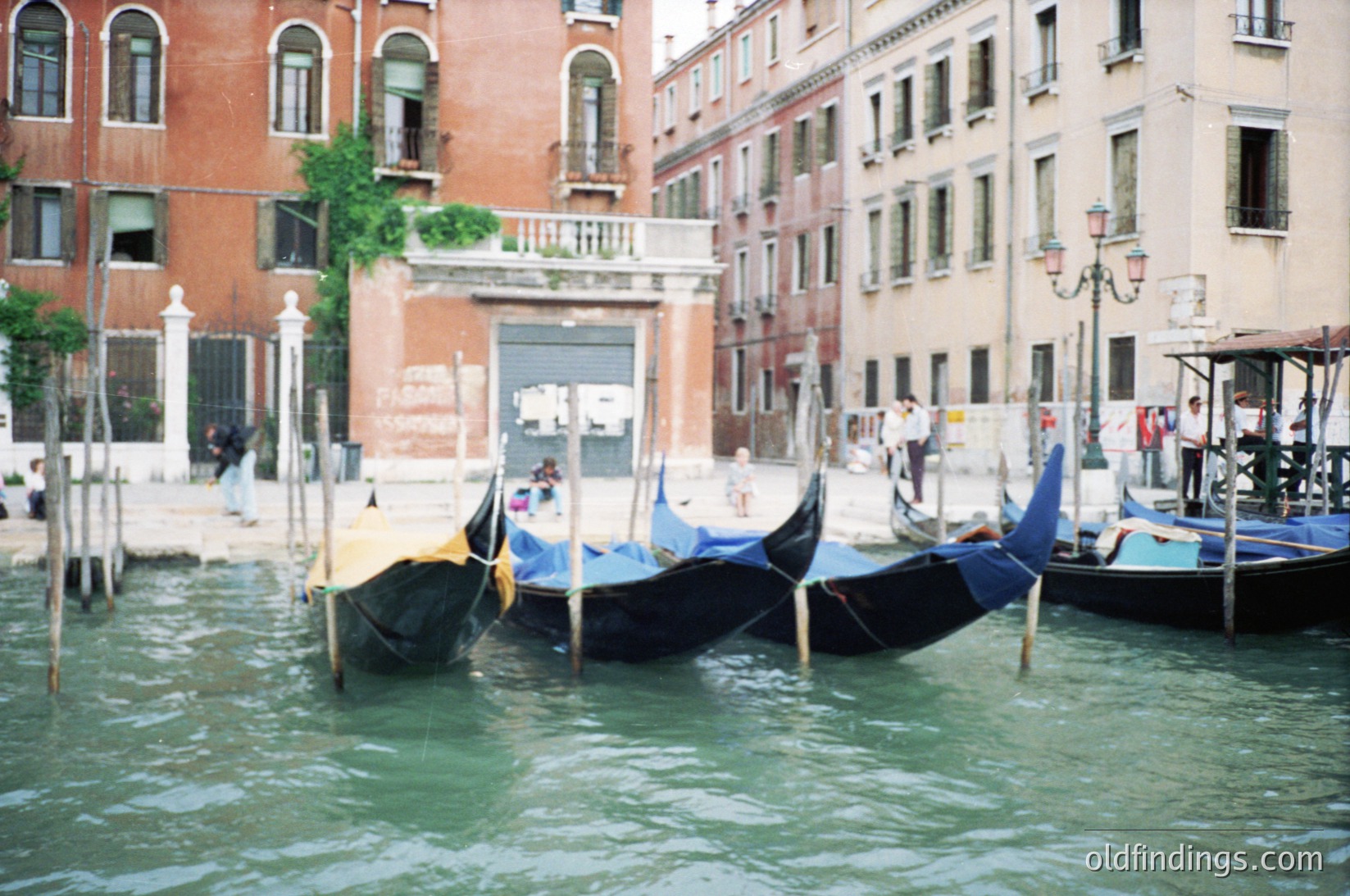 Classic Venetian canal scene with moored gondolas under arched bridges. Historic brick buildings with shuttered windows flank the waterway, reflecting Venetian architecture.