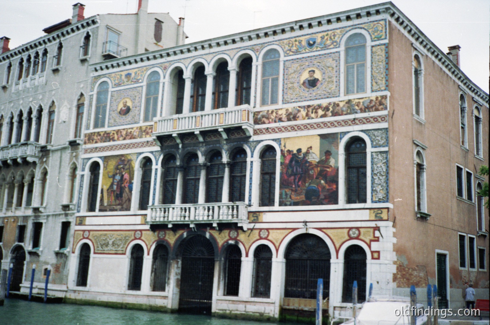 Venetian canal-side palazzo with intricate frescoes depicting historical scenes and religious figures. Architectural details include arched windows, wrought-iron balconies, and decorative stucco. Likely 16th–18th century Venetian Gothic/Renaissance style.