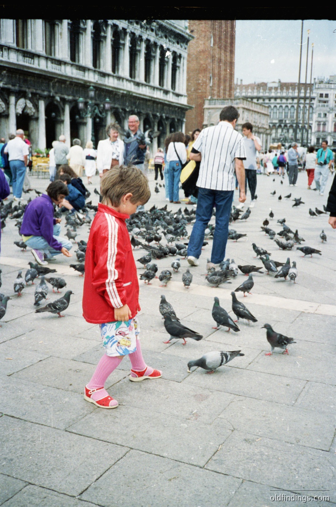 A child in a red Adidas tracksuit stands among a flock of pigeons in St. Mark’s Square, Venice. The 1990s-era clothing and brick-paved plaza suggest a mid-to-late 20th-century tourist scene.