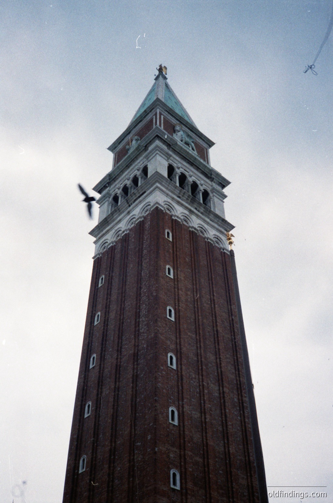Tall brick clock tower with ornate copper dome, featuring rectangular windows and decorative stonework. Likely a historic European landmark, possibly architecture. The structure’s vertical lines and intricate detailing suggest a or influence. #