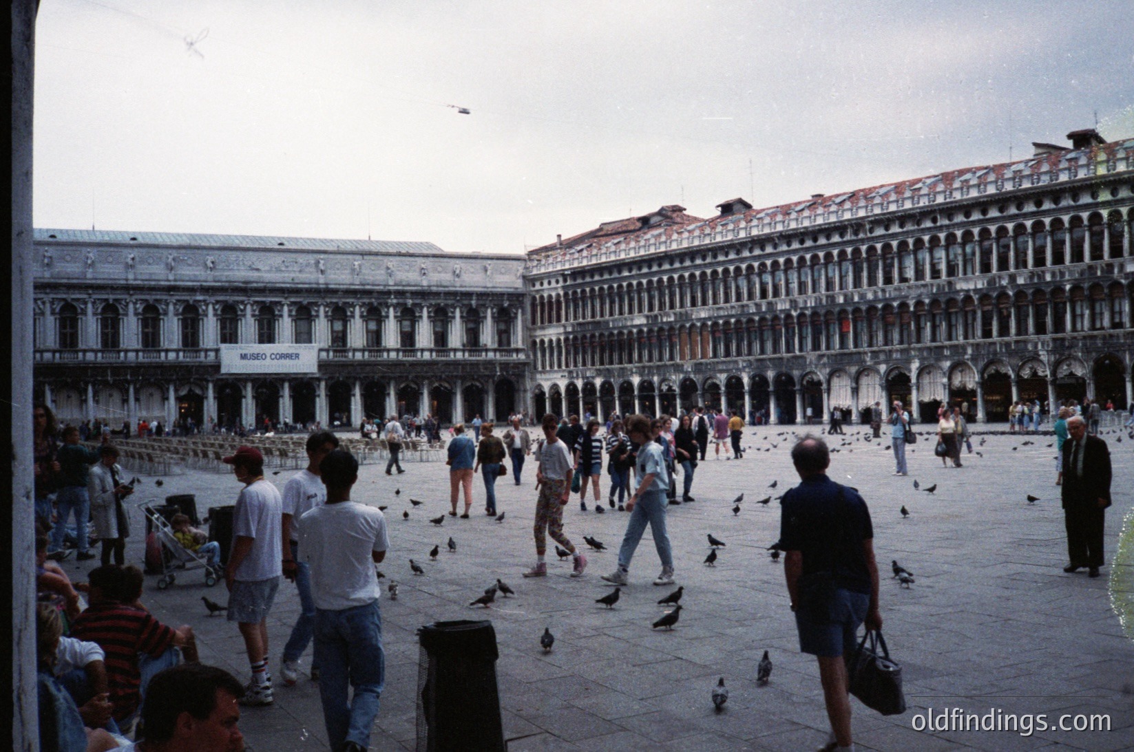 Venetian Piazza with Renaissance-style arcades and pigeons. Crowded square featuring historic (St. Mark’s Square) in Venice, Italy. Mid-20th century attire suggests or . Architectural details include arched colonnades and a visible "Museo Correr" sign.