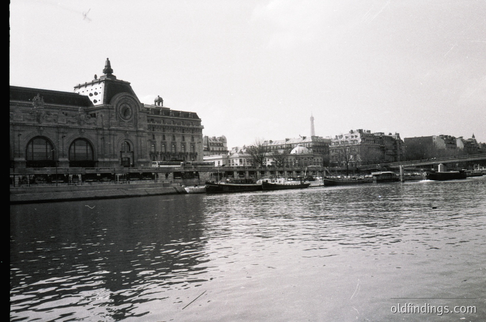 Historic black-and-white view of **Gare de Lyon** railway station in Paris, France, with its iconic clock tower and arched windows. Steamboat docked along the Seine River, mid-20th century (1940s–1960s). Architectural details highlight Art Nouveau influences.
