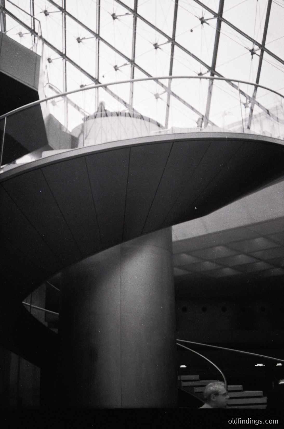 Modernist architectural interior featuring sweeping curved concrete walls and ceiling. Glass-paneled roof allows natural light to flood the space. Minimalist design with geometric precision, likely a public or institutional building from the mid-20th century.