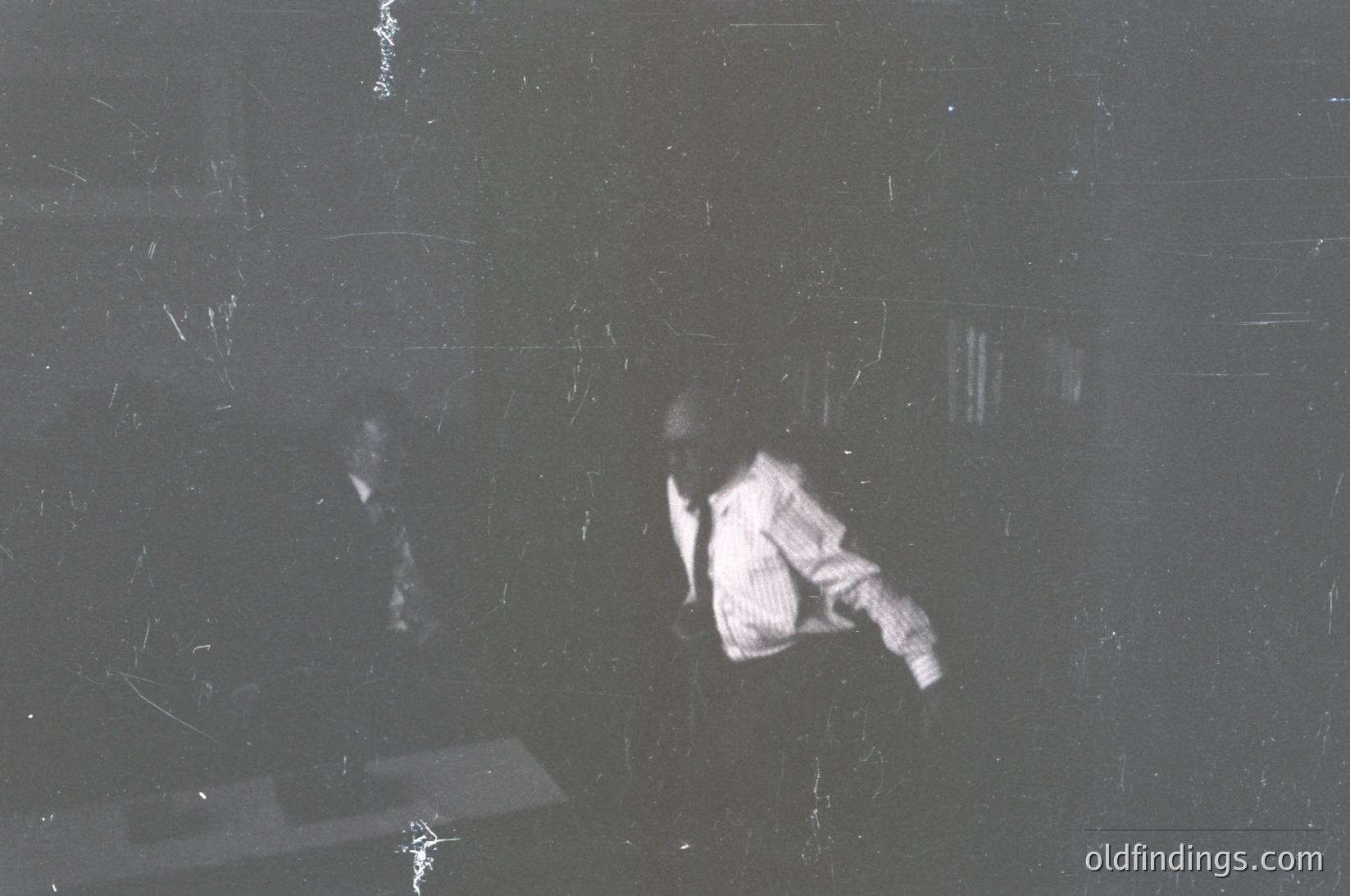 Vintage black-and-white photo of two figures in motion, likely mid-19th to early 20th century. Blurred motion suggests dynamic activity—possibly a dance or theatrical performance. Scratched film grain and uneven lighting enhance nostalgic, historical texture. Potential use for vintage aesthetics, motion studies, or historical research.