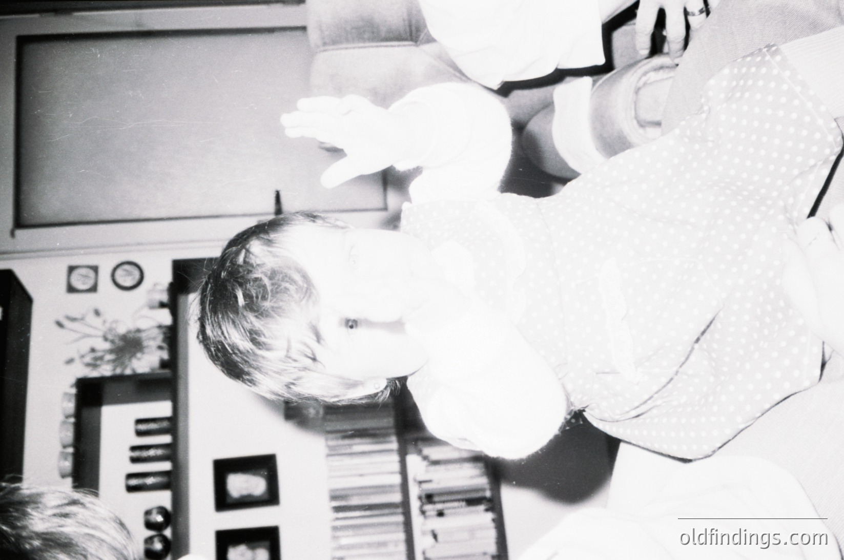 Vintage black-and-white photo of a child peeking from behind a cardboard cutout of a spaceship or rocket, likely from the 1960s–1970s. Decor includes framed posters and shelves with vinyl records, suggesting a mid-century home or classroom setting. Creative play and nostalgia for retro space exploration themes.