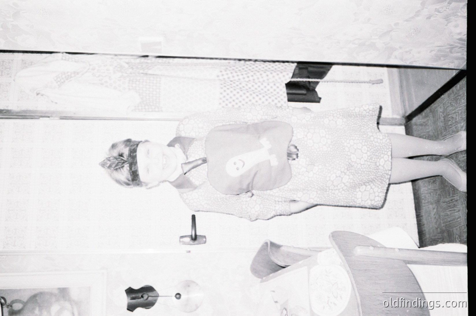 Mid-century modern hotel room interior, captured from a low-angle perspective. A woman in a sleeveless dress sits on a curved, padded bench near a glass-topped table. Minimalist decor includes a wall-mounted lamp and a small, round floor lamp. The setting suggests a 1960s European hotel, likely for stock photography or design references.