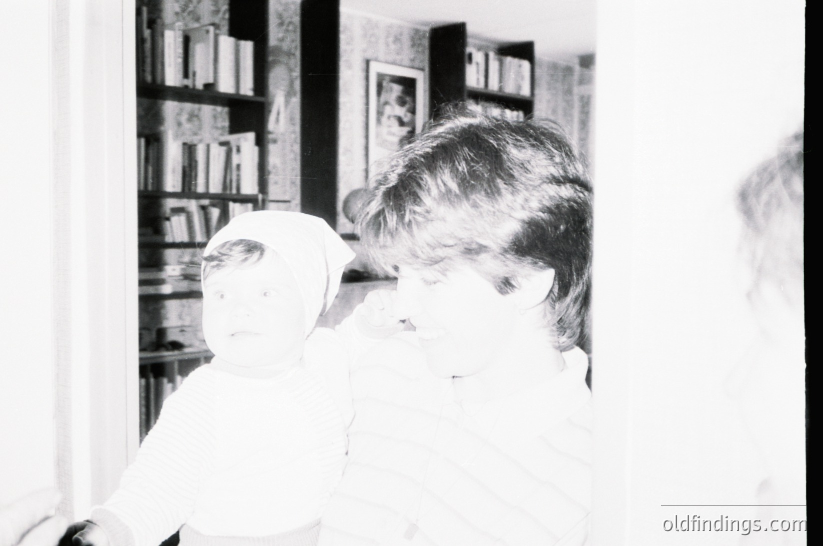 Vintage black-and-white photo of a child in mid-1960s/70s domestic setting, holding a stuffed animal near a bookshelf filled with hardcover volumes. Warm, intimate lighting highlights the child’s focused expression. Ideal for nostalgic or historical research.