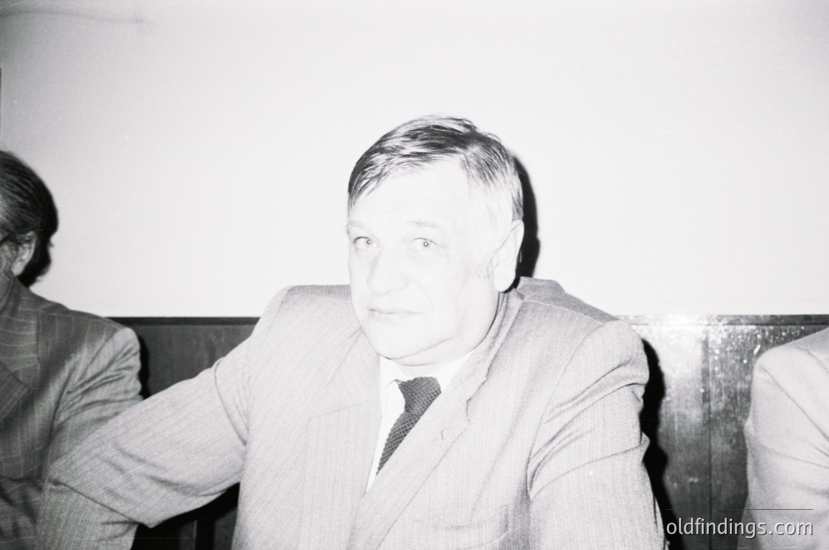 Black-and-white portrait of a man in a formal suit and tie, seated indoors with blurred background. His expression is neutral, and he wears short hair. Style suggests mid-20th century (1950s–1970s) formal attire, likely for professional or official events.