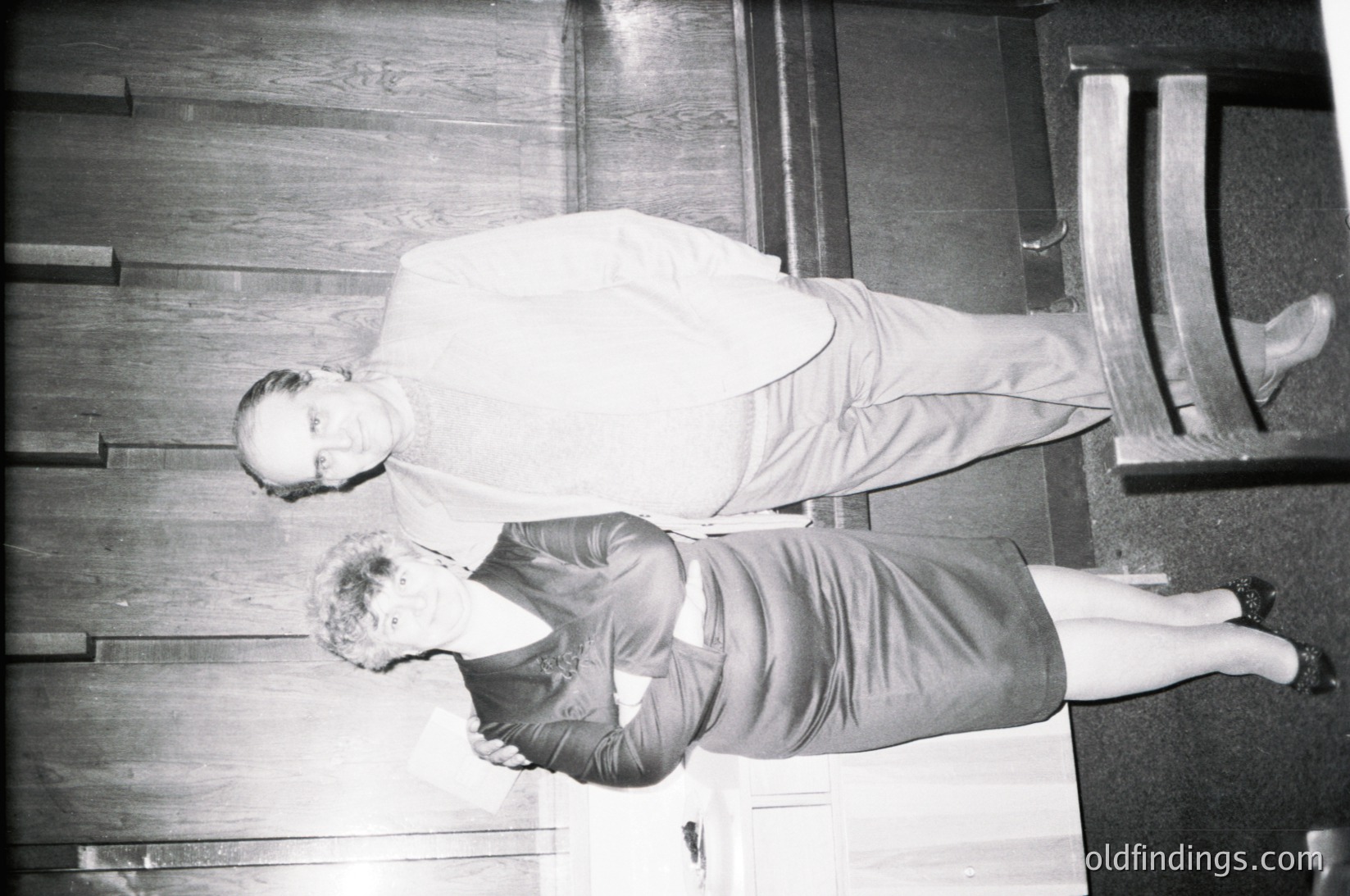 Two individuals in mid-air performing a synchronized stunt on wooden stairs, likely from a 1960s-1970s circus or acrobatics performance. The man in a light-colored shirt and pants and the woman in a dark skirt and top demonstrate precision and athleticism.