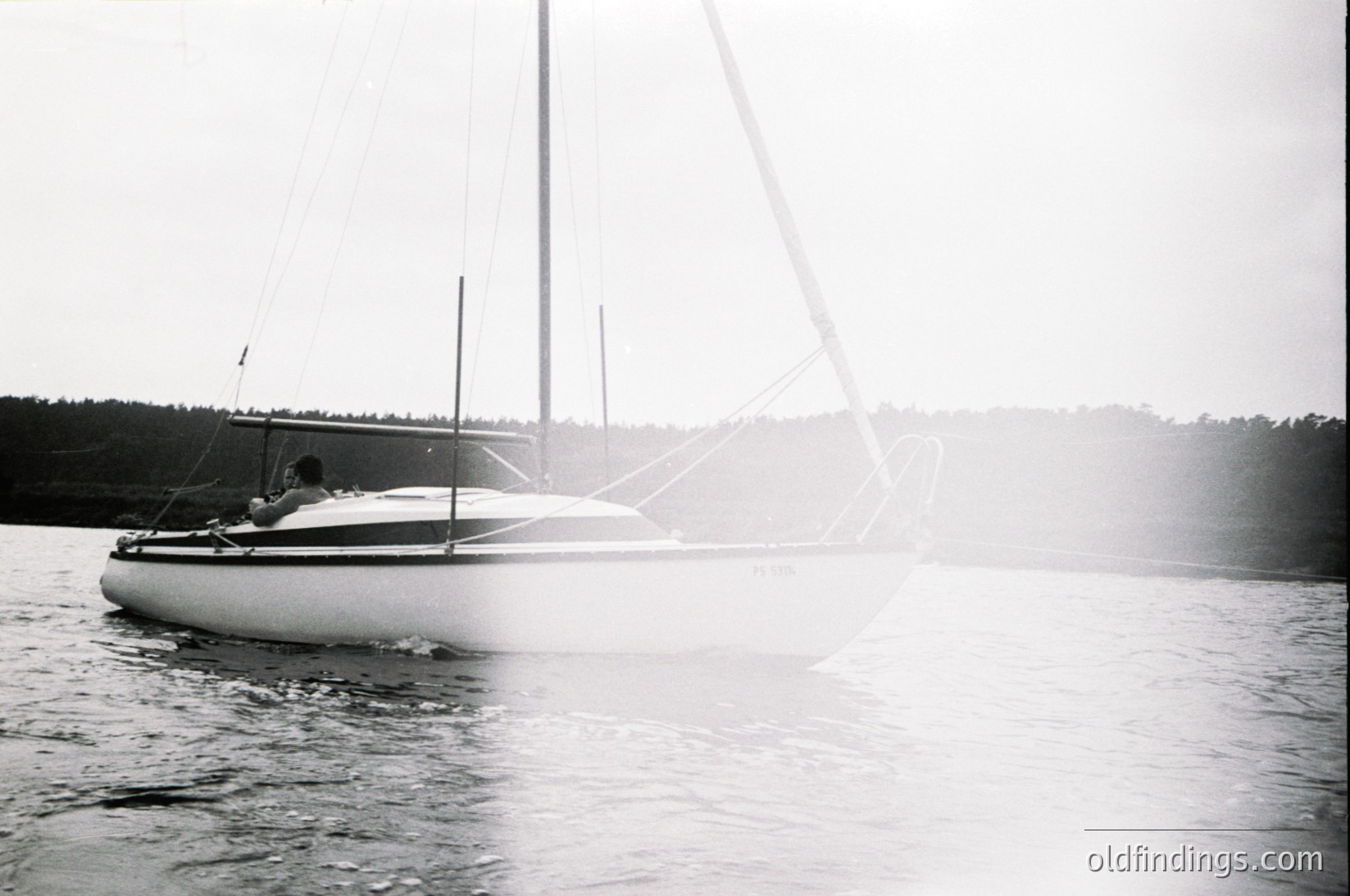 Classic monochrome sailboat cruising on calm waters, likely Baltic Sea or Nordic region. Single person at helm, mid-20th century design with minimalist rigging. Foggy horizon enhances serene maritime atmosphere. Ideal for vintage travel or nautical history research.