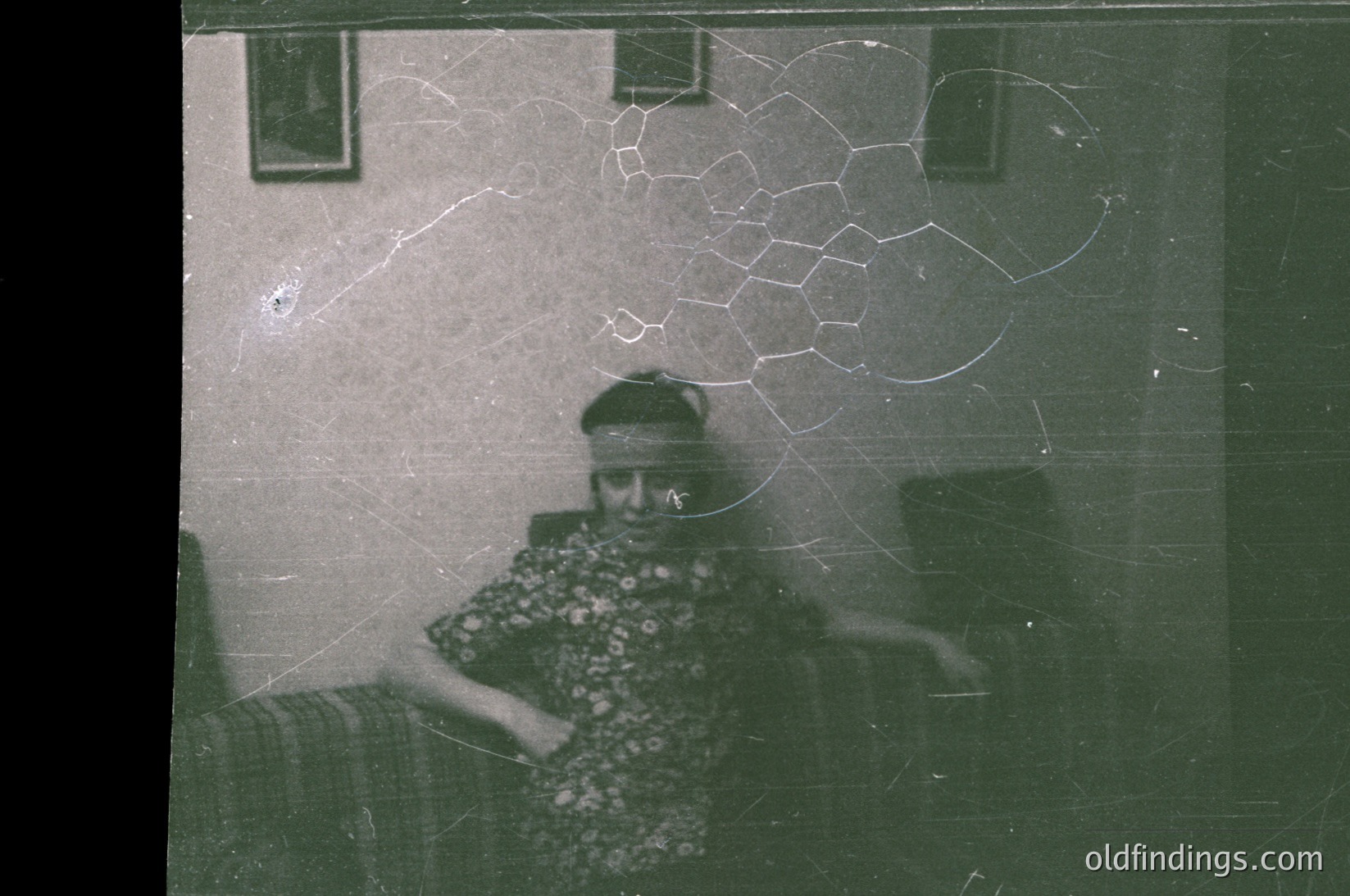 Vintage sepia-toned mirror selfie of an elderly woman in patterned blouse, seated indoors. Cracked mirror surface reveals a window with light and a partial view of a room. Likely mid-20th century domestic setting.