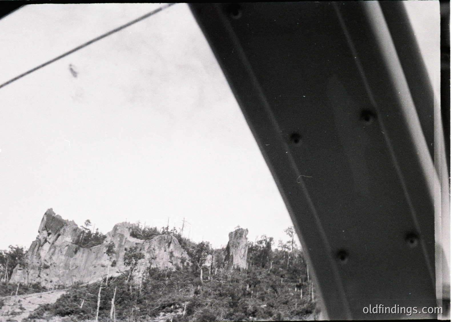 Black-and-white aerial view of rugged limestone formations and dense foliage, likely part of a historic or archaeological site. The perspective suggests a low-angle shot from a vintage aircraft, with visible rivets and structural details of the wing frame.