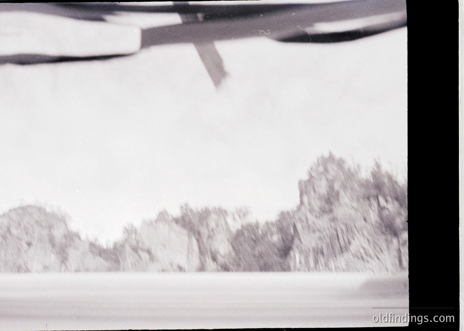 Vintage black-and-white aerial shot of snow-covered mountainous terrain, likely captured mid-flight. Blurred horizon suggests motion or low shutter speed. Potential alpine or polar region setting.