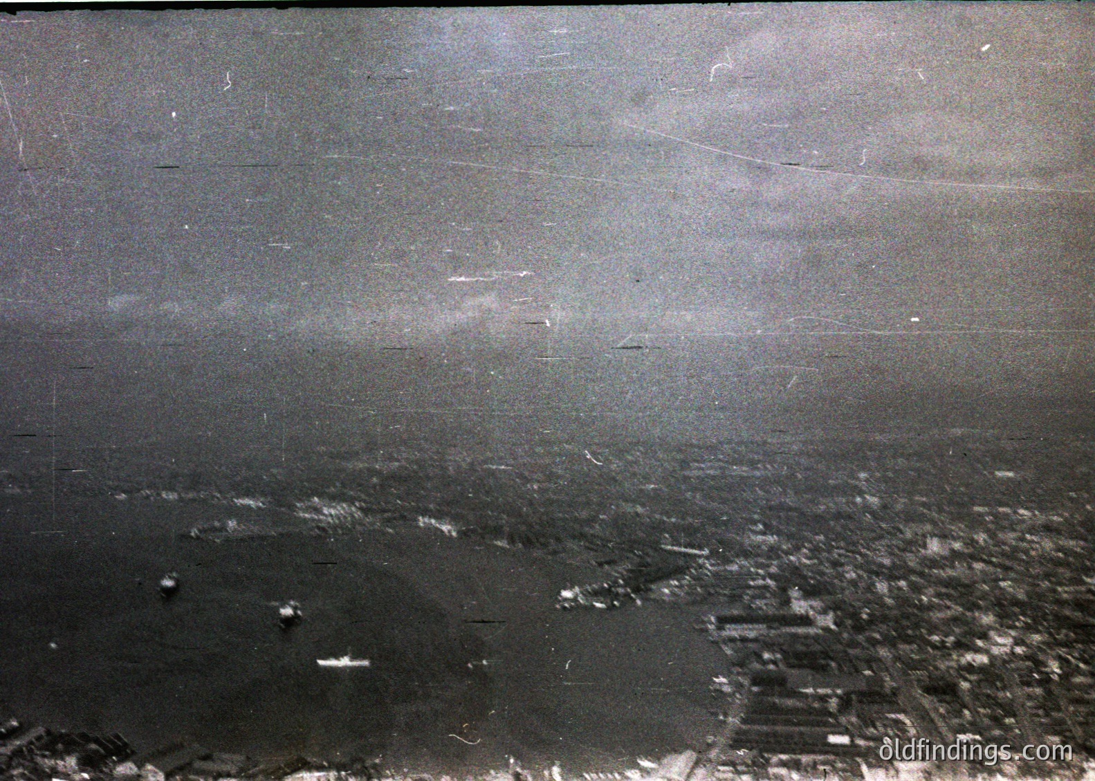 Aerial black-and-white photo of a coastal cityscape, likely from the early-to-mid 20th century. Dense urban grid meets a sprawling harbor with visible docks and ships. Industrial buildings line the waterfront, while residential areas extend inland.