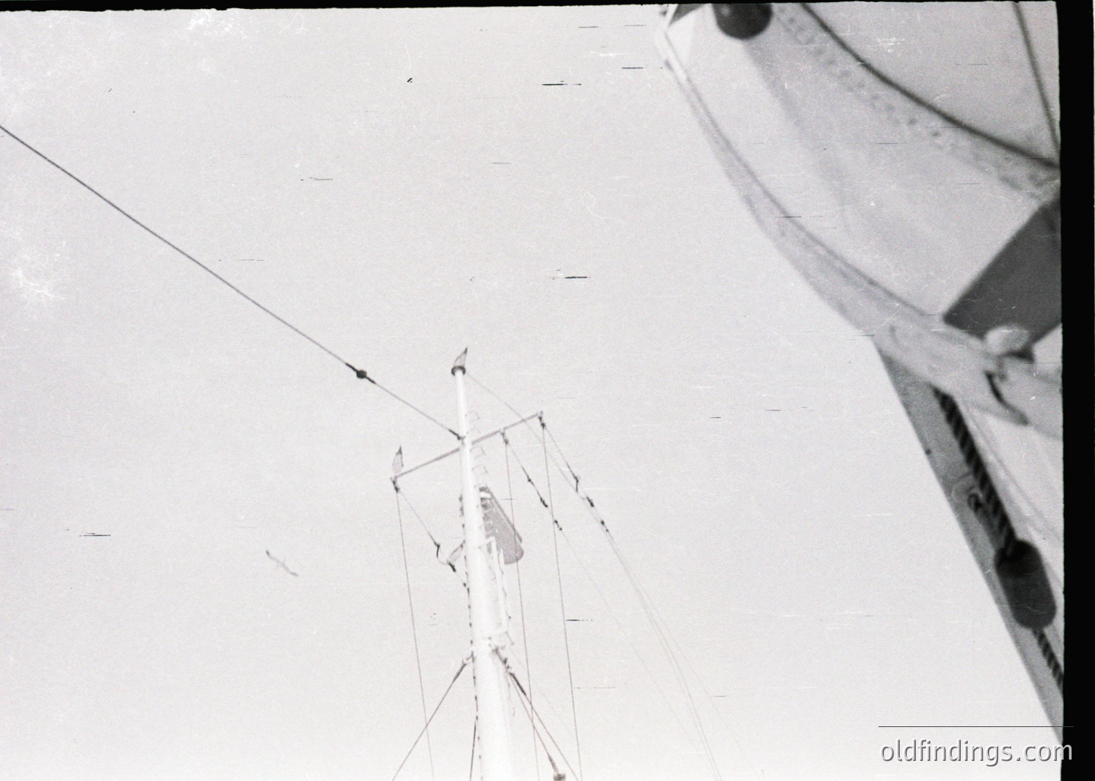 Aerial view of a lone figure ascending a tall, triangular metal framework on snow, likely a ski lift or research structure. The individual wears a backpack and climbing gear, suggesting alpine exploration or scientific activity. Mid-20th century outdoor photography.