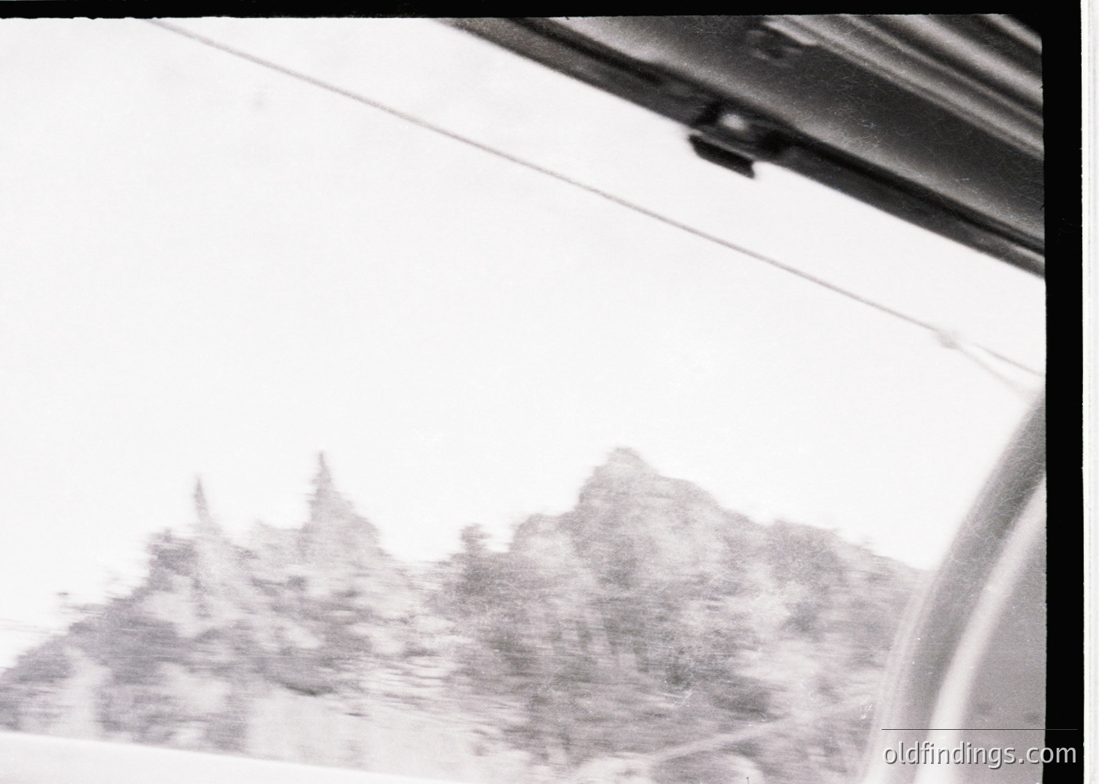 Vintage black-and-white shot of rugged alpine peaks viewed through a car window, suggesting mid-20th century travel. Distorted lens effect highlights nostalgic, candid style. Ideal for vintage travel or automotive history archives.