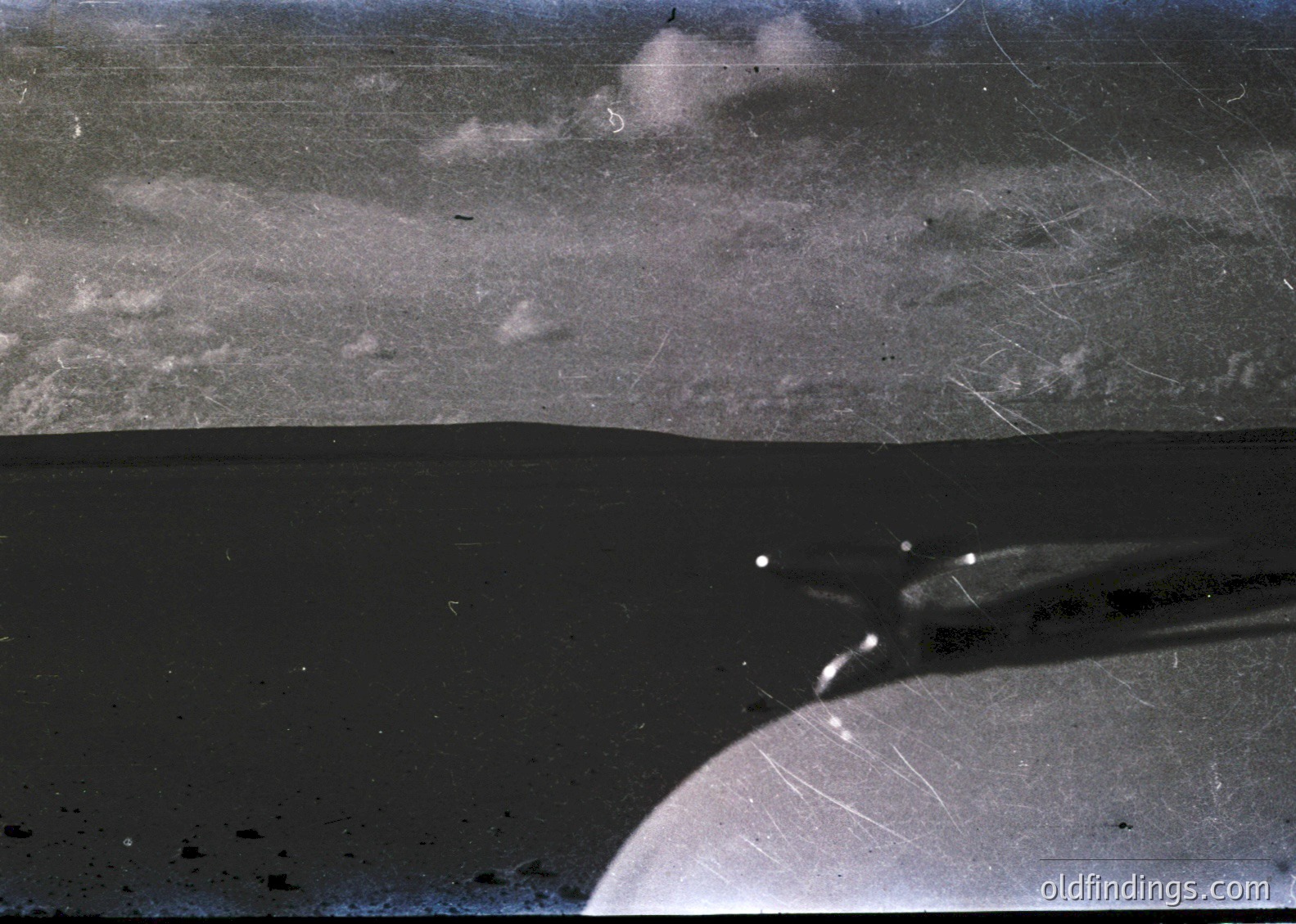 Vintage aerial photo of a coastal landscape with low-lying clouds and mist. The horizon reveals a dark shoreline with subtle wave action. Likely mid-20th century due to film grain and sepia tone.