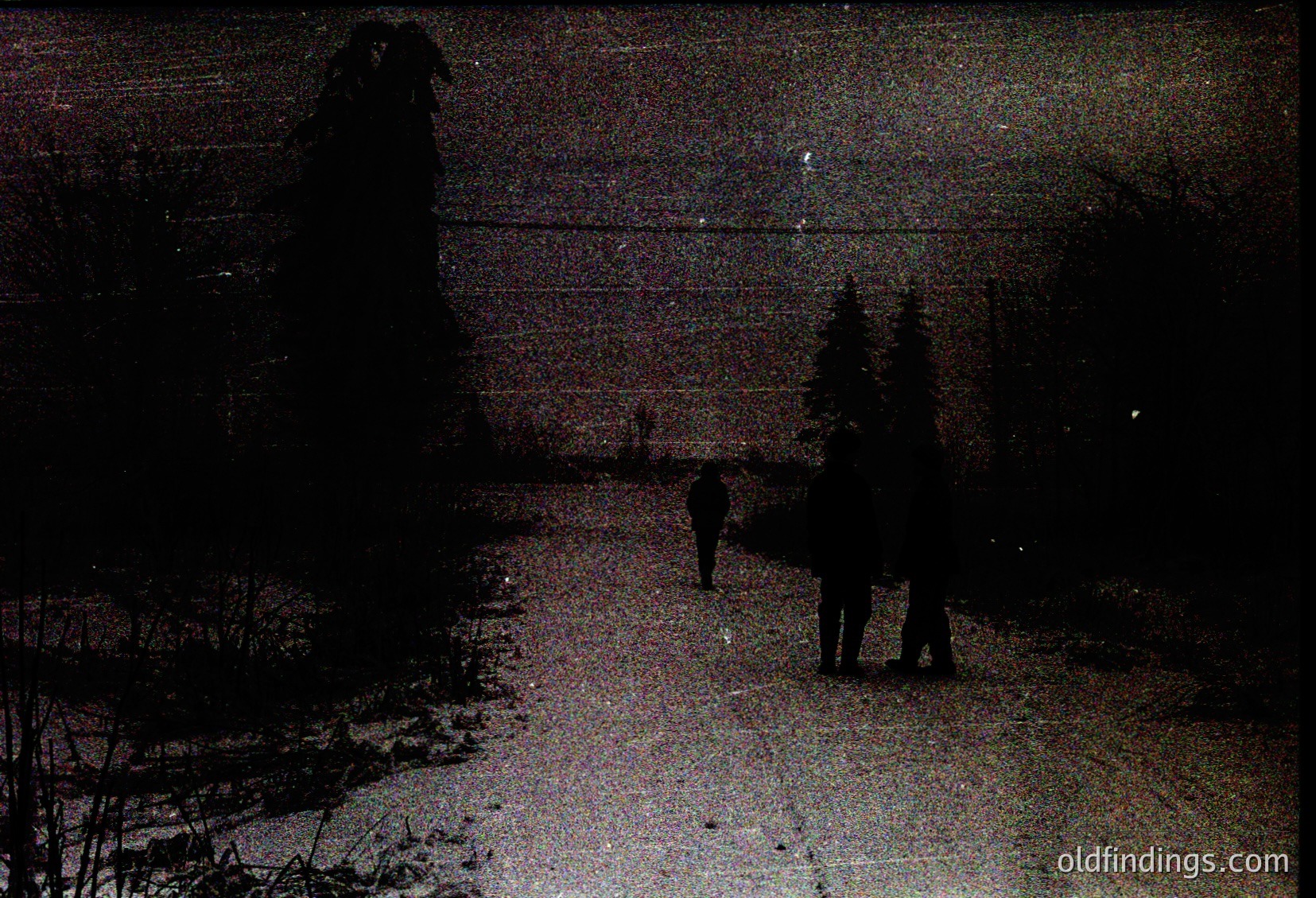 Vintage sepia-toned street scene at dusk, featuring three silhouetted figures walking away from camera. Urban setting with bare trees, utility poles, and a faintly visible brick wall. Likely mid-20th century () due to lighting and composition.