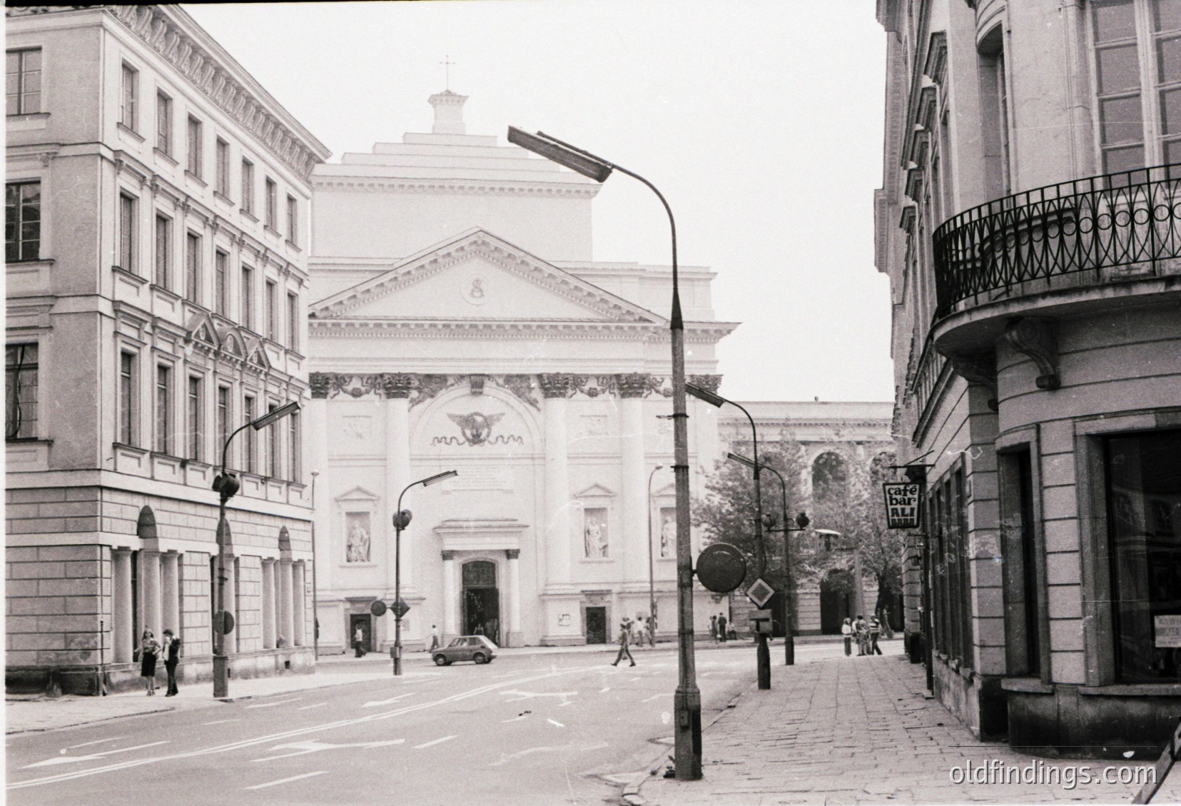 Neoclassical urban plaza featuring grand entrance archway with "МАРКС" signage, flanked by symmetrical stone buildings. Pedestrians and vintage streetlamps add to the historic European street scene. Likely Bulgaria, 1960s–1980s.