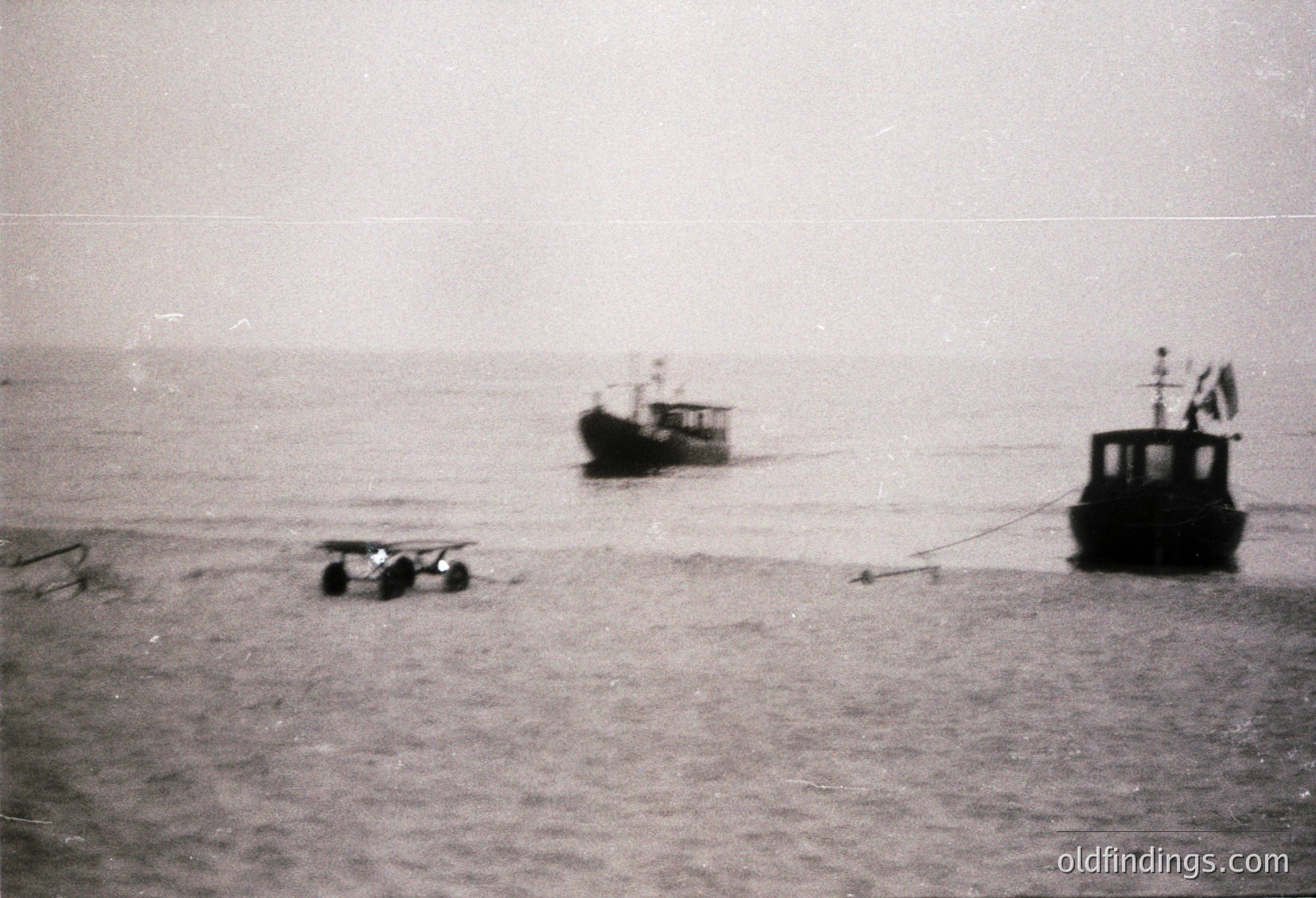 Vintage black-and-white coastal scene featuring two small fishing boats anchored near a weathered pier. One boat displays a flag, suggesting maritime activity. Foggy horizon enhances nostalgic atmosphere. Likely mid-20th century.