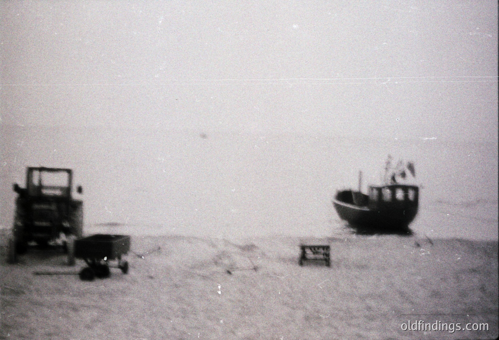 Vintage black-and-white beach scene featuring a small wooden boat, cart, and crate on sandy shore. Minimalist composition suggests early-to-mid 20th century coastal life. Ideal for historical research or nostalgic design references.