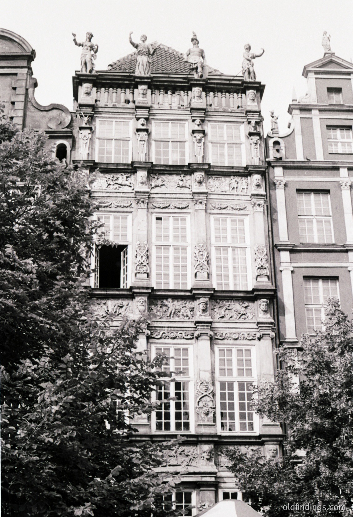 Baroque-style building facade with intricate stone carvings, statues, and symmetrical windows. Ornate reliefs depict classical figures and floral motifs. Likely European, 17th–18th century.