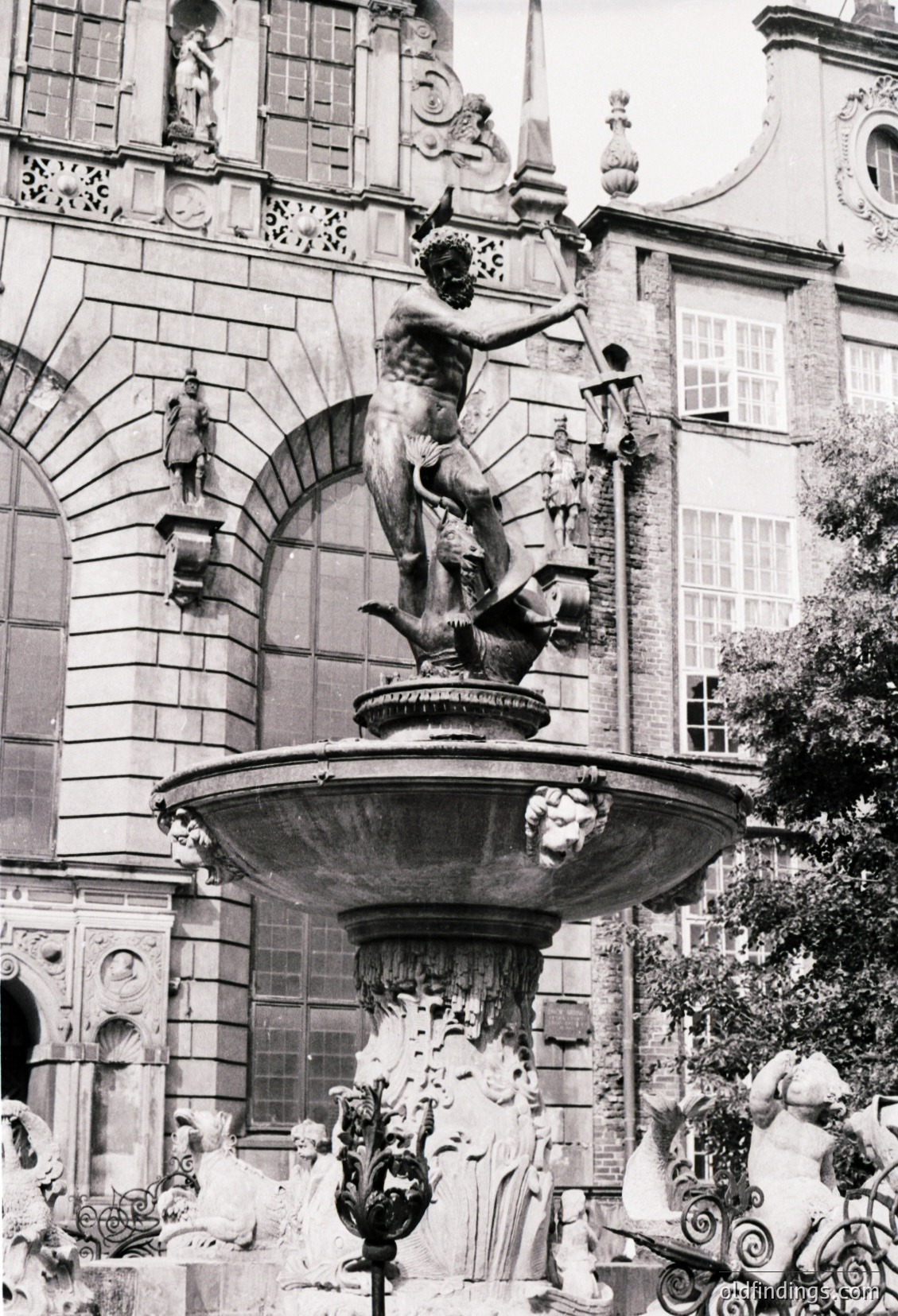 Baroque-style fountain featuring a central male figure treading a sea creature, surrounded by intricate carvings and decorative elements. Architectural details include arched niches and ornate stonework. Likely European, 17th–18th century.