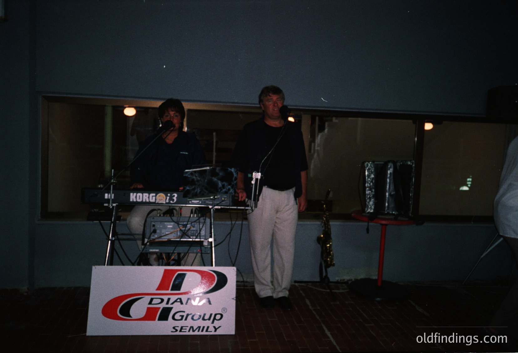 Live band performance featuring a keyboardist (Korg M3) and saxophonist on stage, likely 1990s. Sign reads "Diana Group Semily," suggesting a regional or local event. Indoor venue with minimal lighting, emphasizing the performers.