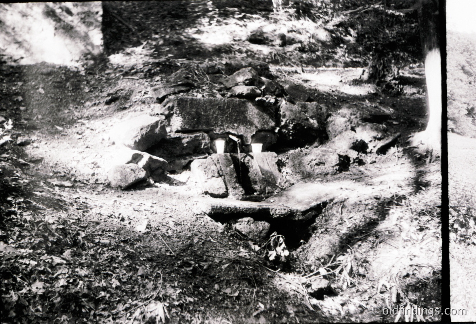 Ruined concrete structure partially buried in overgrown forest terrain, likely post-war or abandoned. Distinctive rectangular concrete blocks and exposed rebar suggest mid-20th century construction.