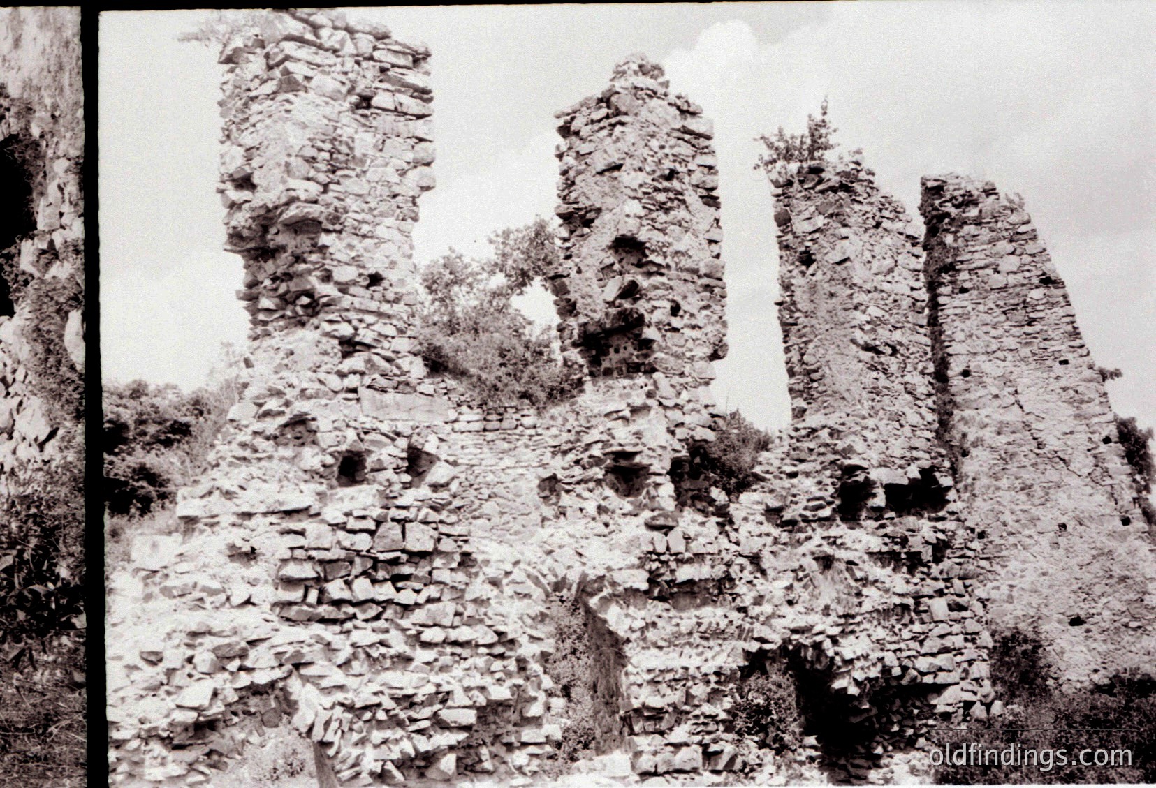 Ruins of stone towers with weathered brickwork and arched windows, likely remnants of a medieval fortress. Vegetation partially covers the base. Black-and-white sepia tone suggests vintage photography, possibly late 19th to early 20th century.