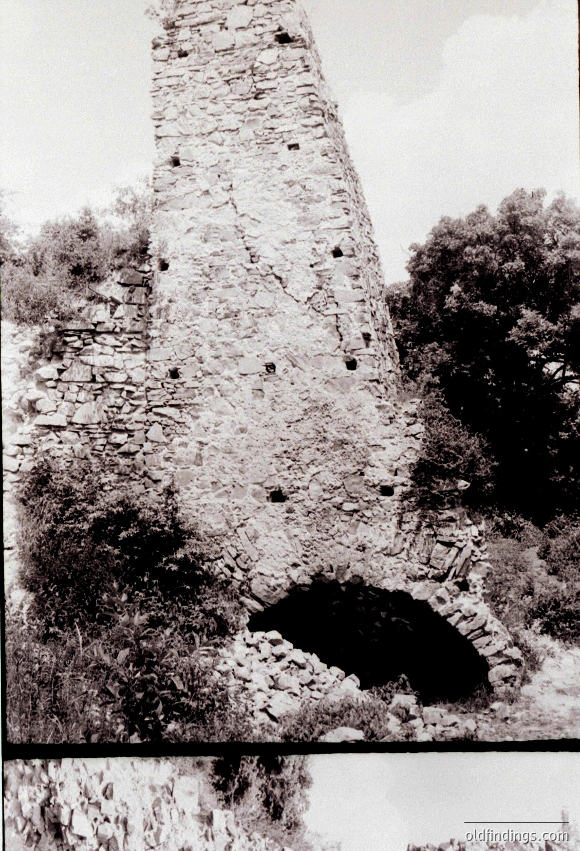 Ruined stone tower with visible arched doorway, likely medieval fortress remains. Weathered bricks and overgrown foliage suggest abandonment.