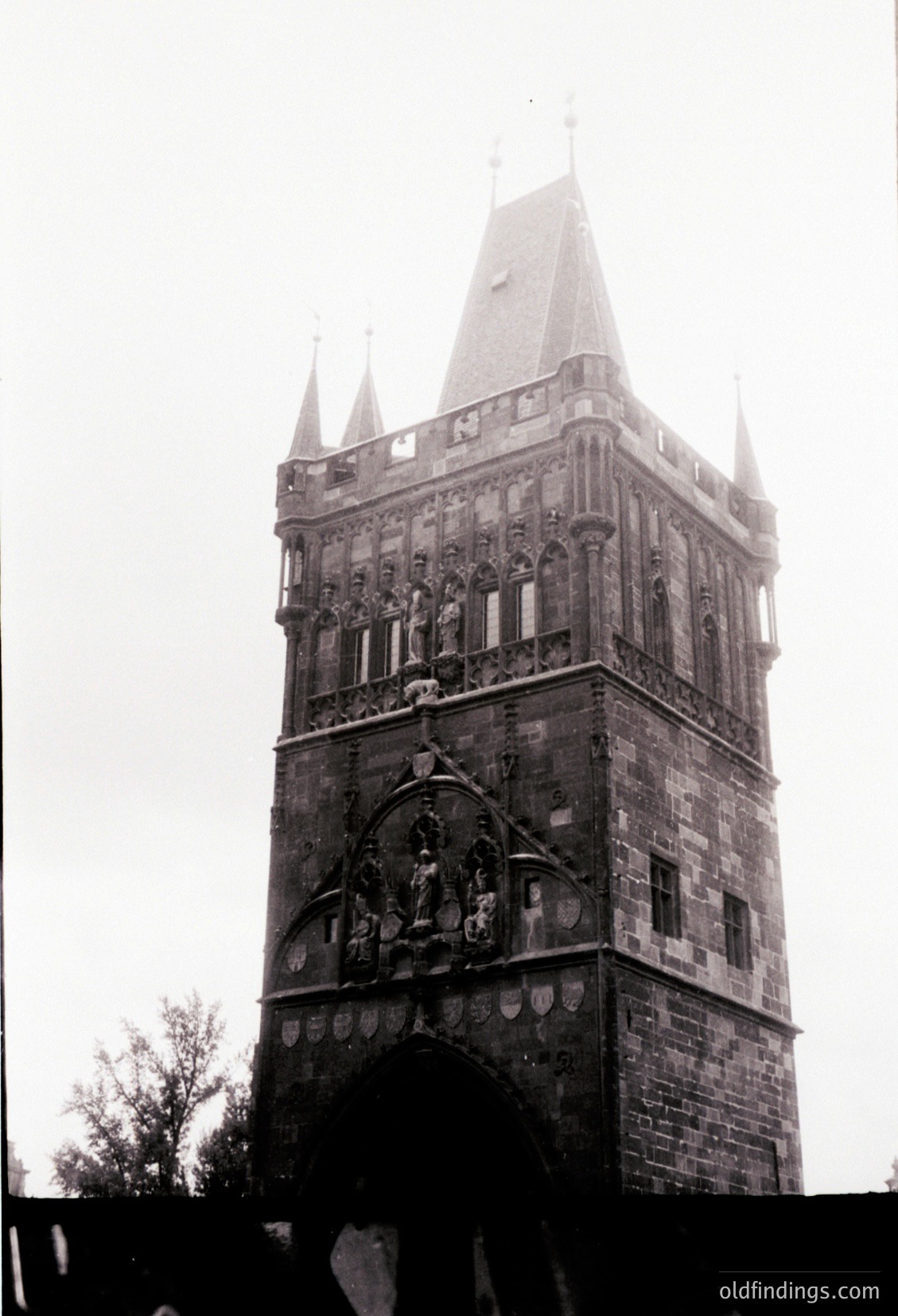Historic stone tower with Gothic Revival architecture, featuring ornate carvings and a pointed spire. The central relief depicts a coat-of-arms or heraldic emblem. Likely European, mid-19th century.