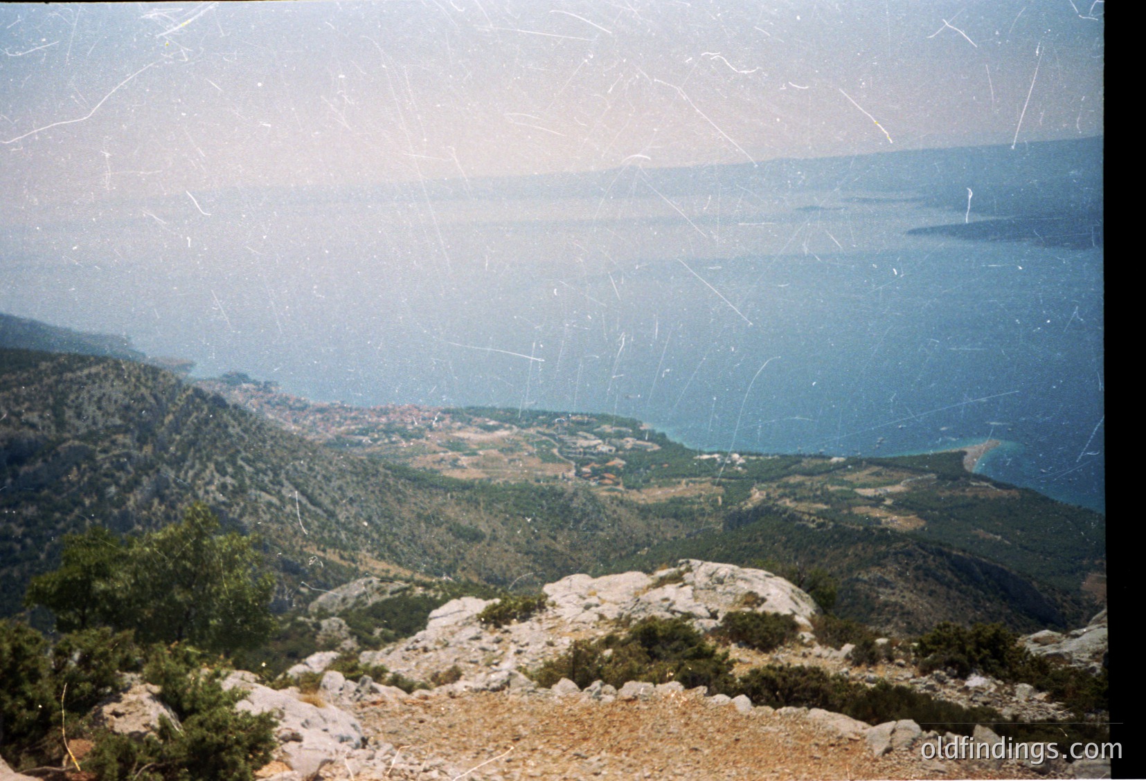 Vintage panoramic shot of rugged coastal terrain with layered hills, rocky outcrops, and distant sea. Evidence of age: scratches, fading, and slight film grain. Likely Mediterranean or Adriatic region.