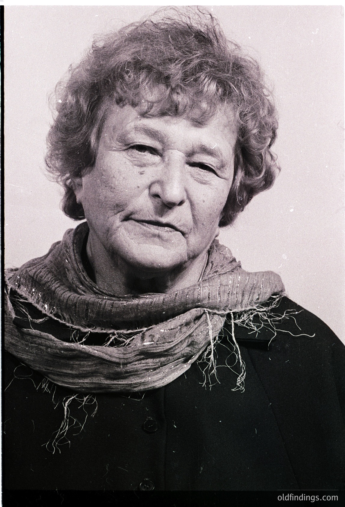 Portrait of an elderly woman in mid-20th century attire—gray scarf, dark blazer, and short hair. Grainy black-and-white suggests vintage photography, likely 1950s–1970s. Neutral expression conveys timelessness.