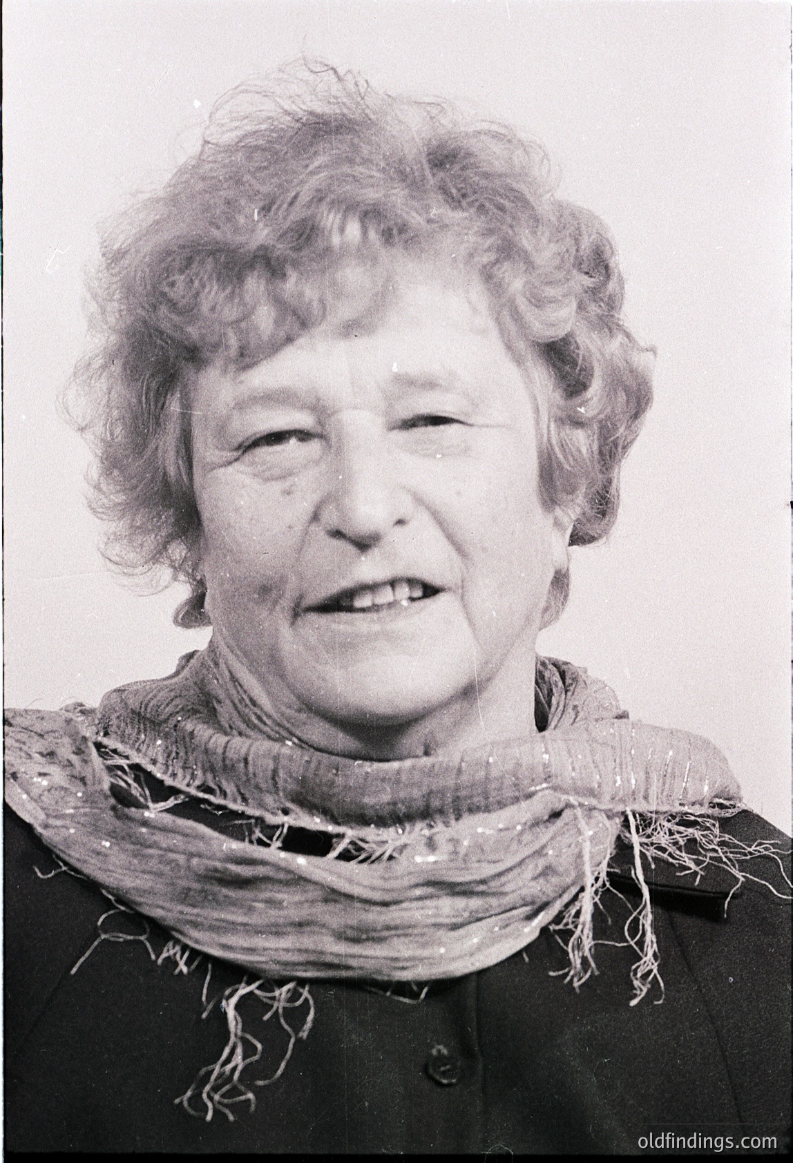 Portrait of an elderly woman in mid-20th century attire, likely 1950s–1960s. She wears a dark jacket with a frayed, textured scarf draped around her neck. Soft focus and candid expression evoke warmth and timelessness.