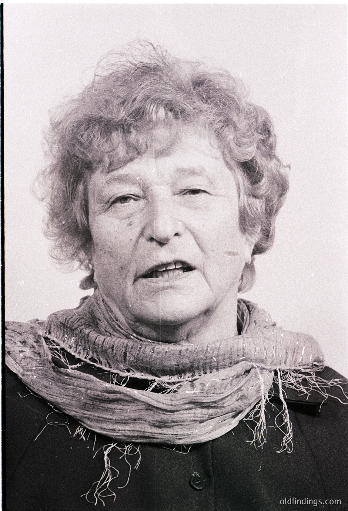 Portrait of an elderly woman in mid-speech, wearing a textured scarf and dark jacket. Black-and-white, likely mid-20th century (1950s–1970s). Expression conveys intensity.