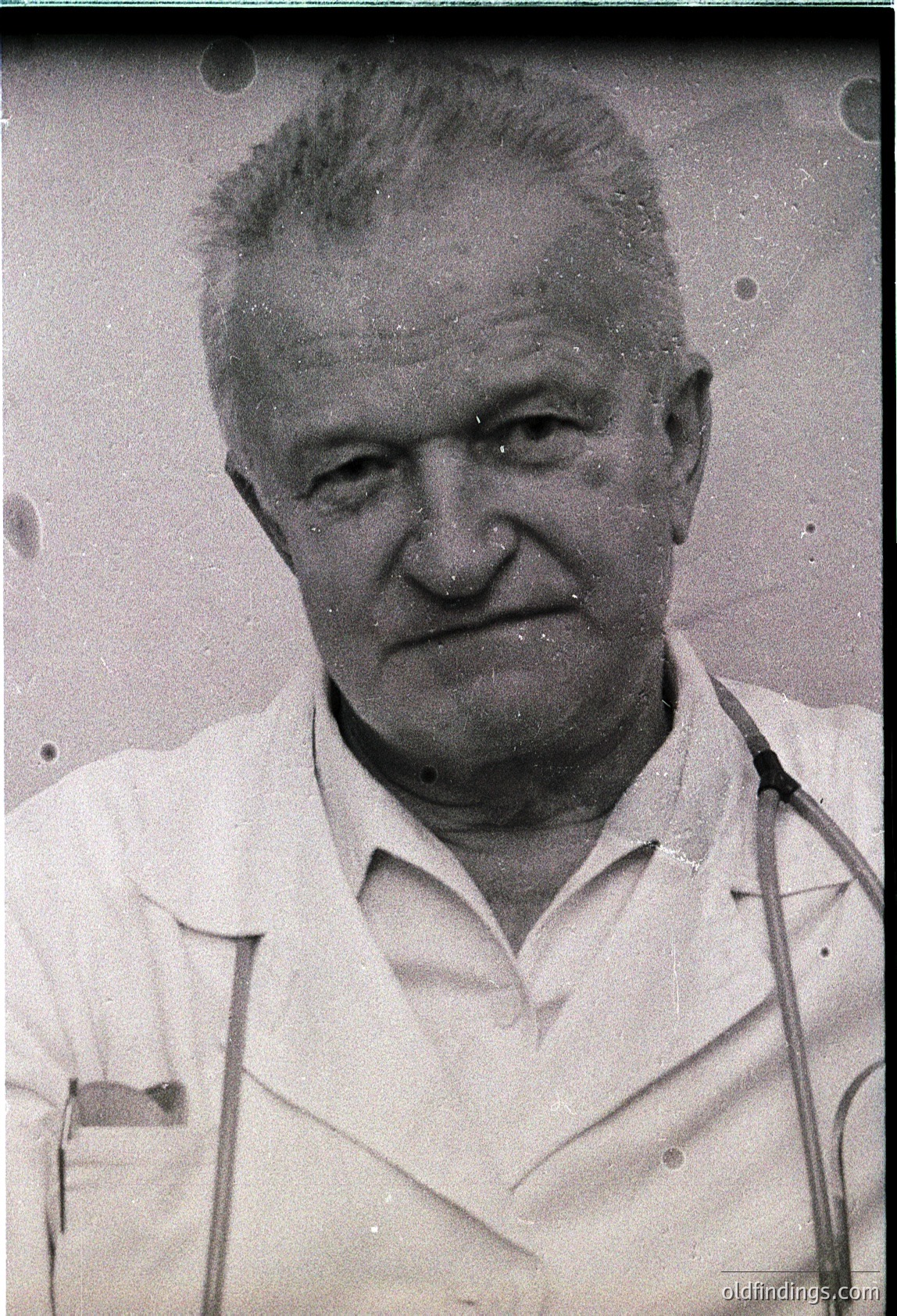 Mid-century black-and-white portrait of an elderly man in a white lab coat, likely a physician or scientist. His expression is neutral, with short, receding hair. The grainy texture and lighting suggest a vintage studio photograph from the **1950s–1960s**.