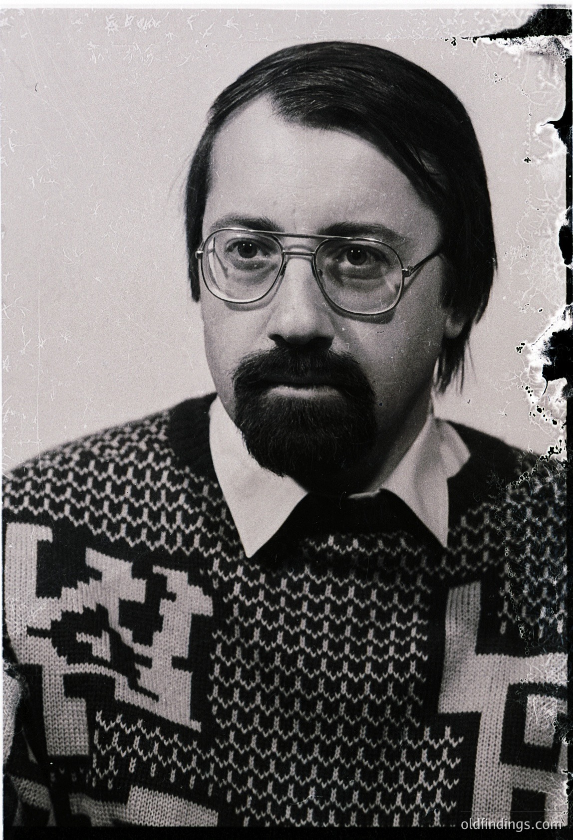 Portrait of a man in a patterned sweater and round glasses, likely from the 1970s–1980s. Geometric, textured knit suggests mid-century fashion trends. Neutral background enhances focus on facial expression and attire.