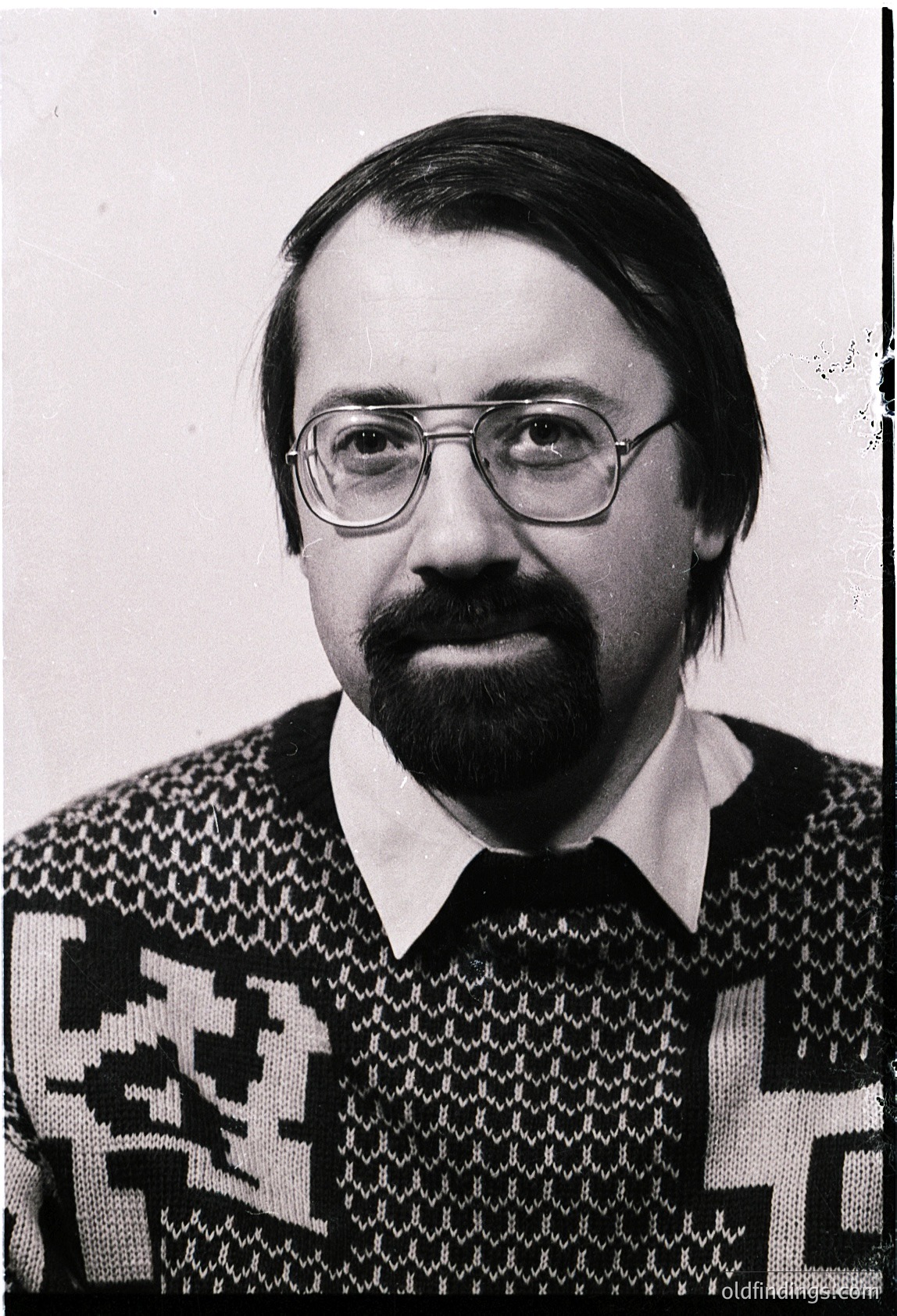 Portrait of a man in a patterned sweater, likely from the 1970s–1980s. Geometric, abstract textile design with bold black-and-white contrast. Glasses with rectangular frames. Plain background suggests studio or formal setting.