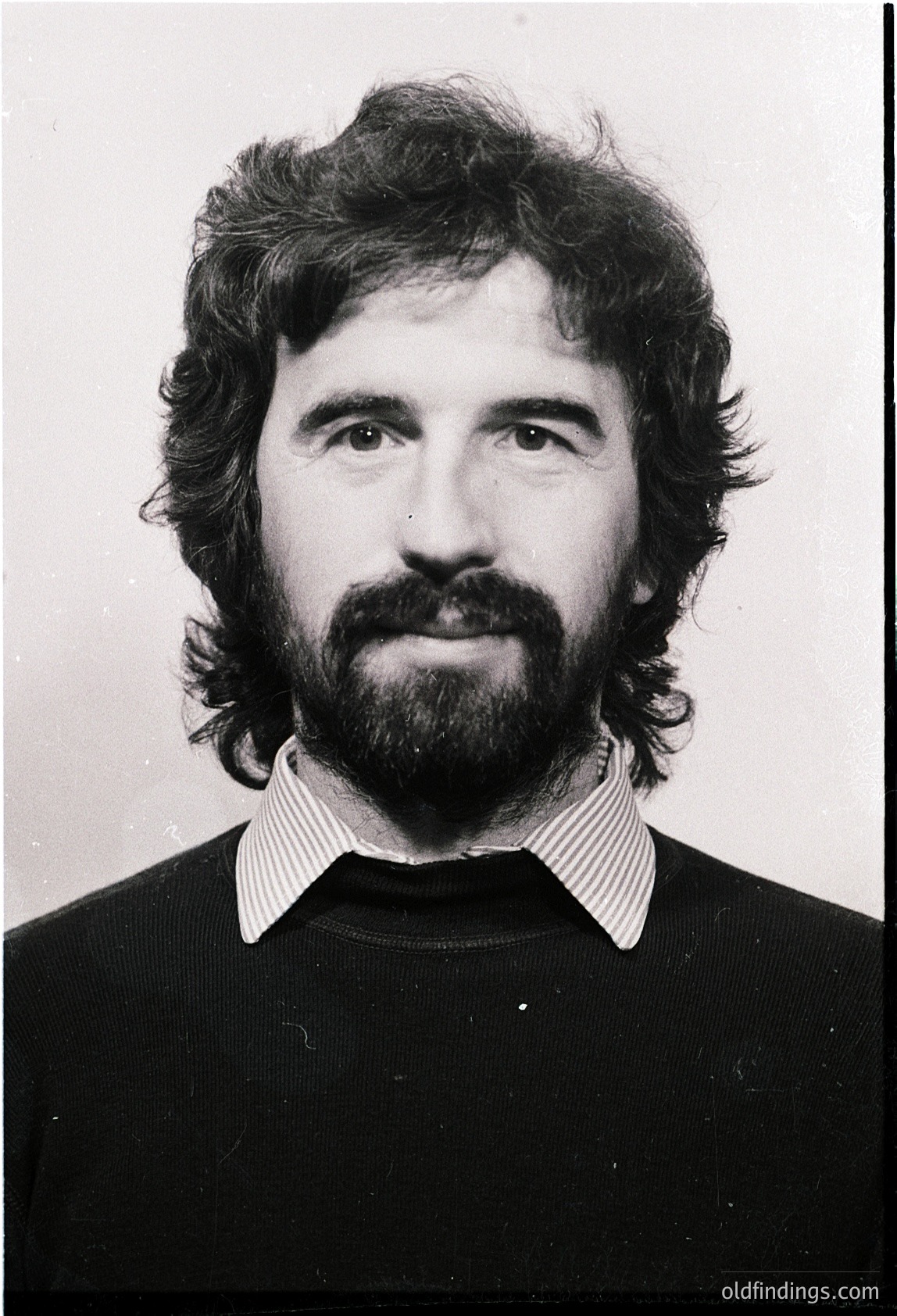 Portrait of a man with a full beard and mustache, wearing a striped collared shirt and dark sweater. Style suggests mid-20th century professional or identification photography.