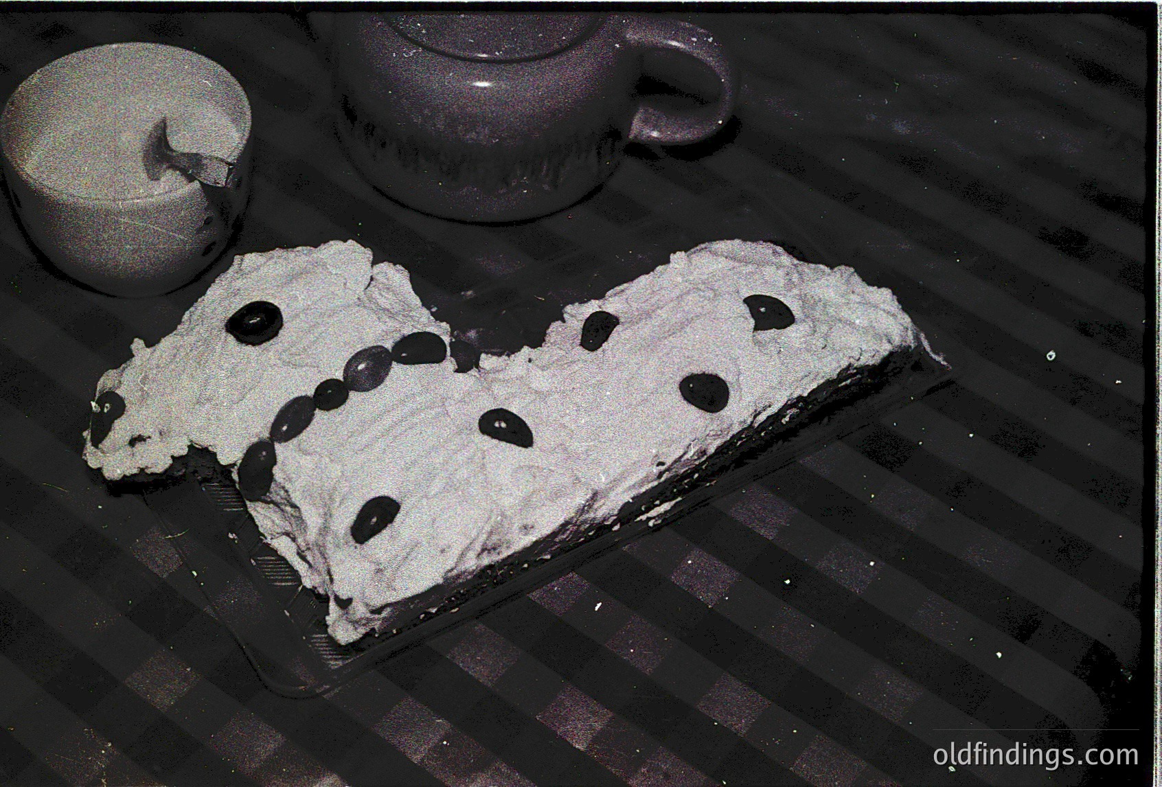 Homemade layered cake with white icing and blackcurrant decorations on a striped tray, beside a ceramic pitcher and glass of milk. Classic dessert presentation.