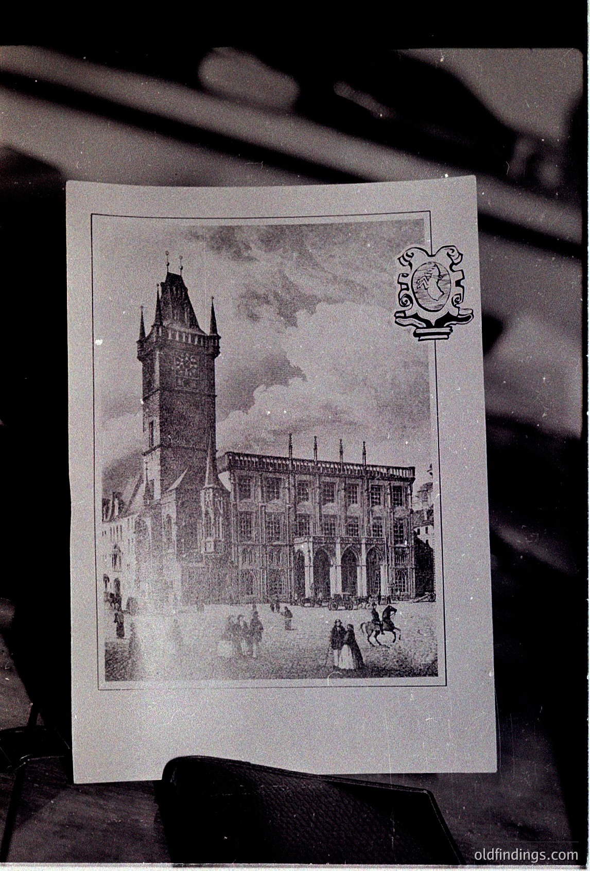 Vintage postcard featuring a grand 19th-century European clock tower with Gothic Revival architecture. Symmetrical facade with arched windows, a central entrance, and a square tower topped with a spire. Crowd of people and horse-drawn carriages in the courtyard below. Likely from a city like Prague or Vienna.