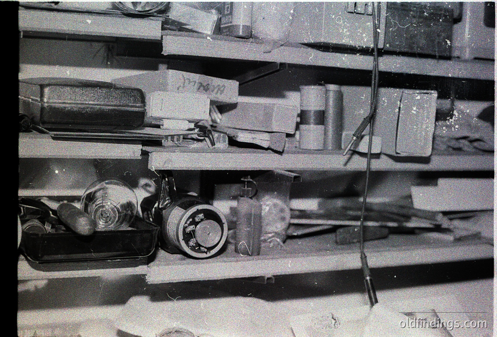 Vintage industrial shelf stocked with cylindrical metal containers, valves, and mechanical parts. Possible mid-20th century factory or workshop setting. Items appear aged, suggesting historical or archival value.