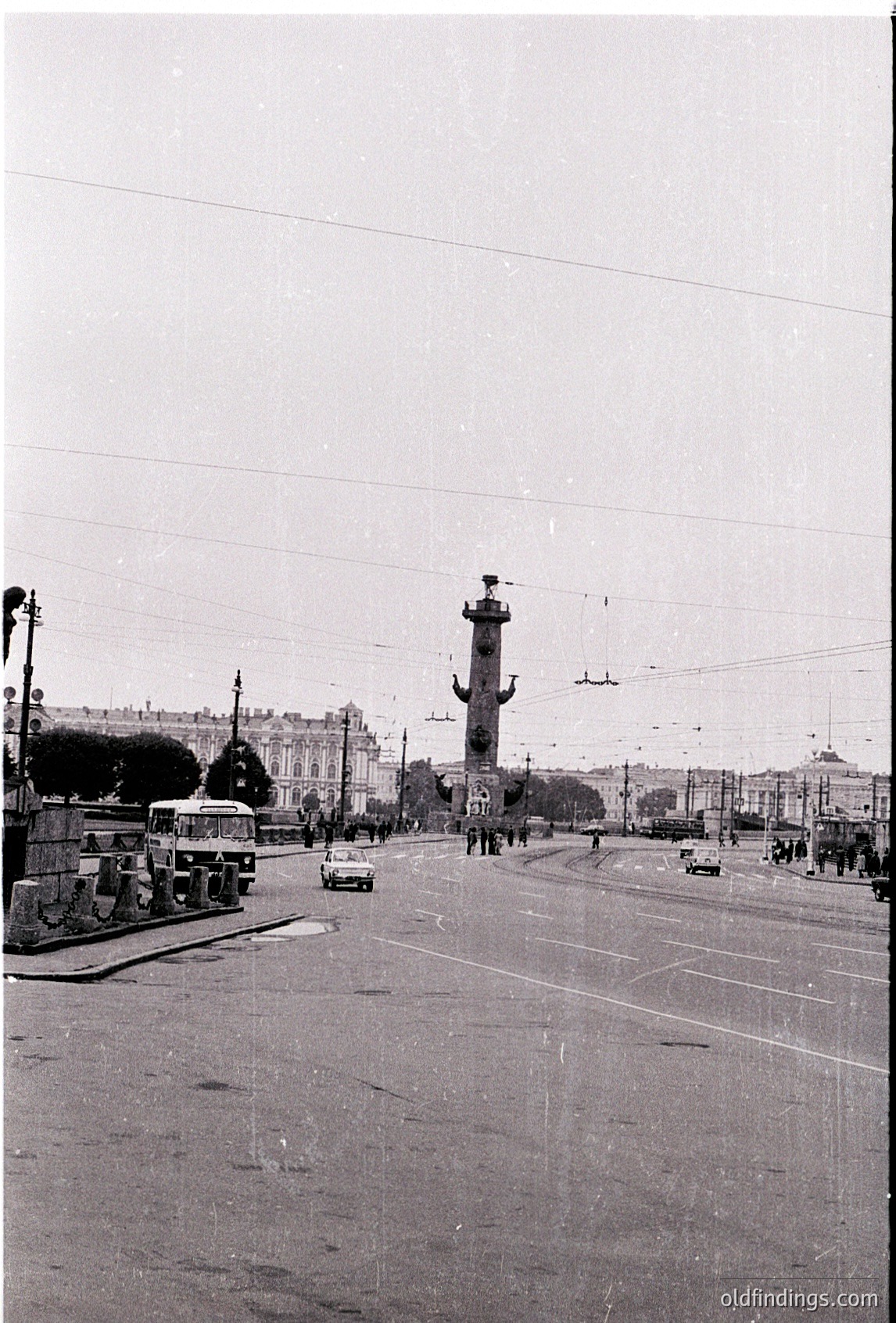 Mid-20th century urban scene featuring a prominent column monument in a wide boulevard. Soviet-era architecture with tram lines, vintage cars, and pedestrians. Likely Moscow’s **Dzerzhinsky Square** (1950s–60s).