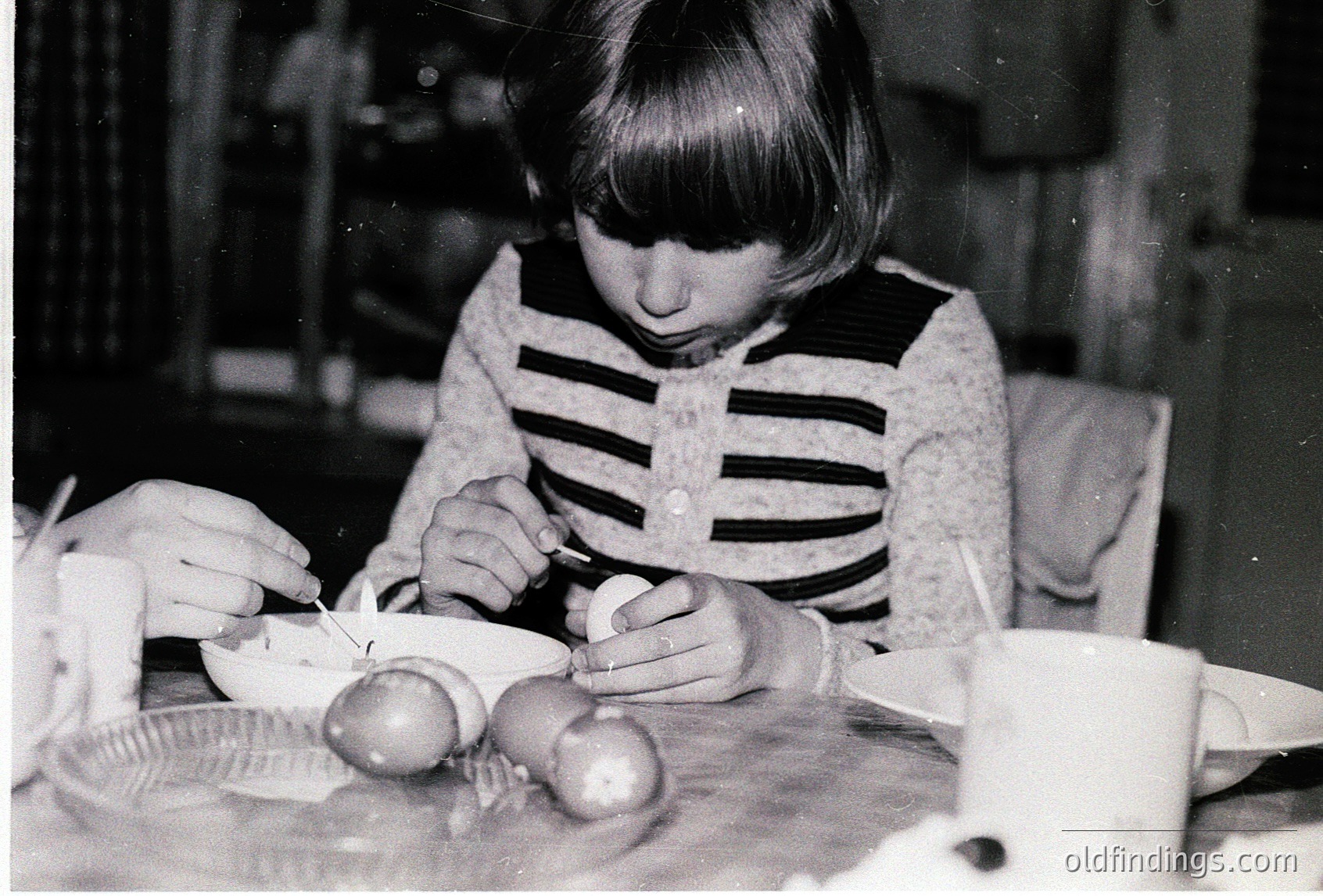 Young girl peeling hard-boiled eggs at a table, mid-1960s–70s domestic setting. Vintage striped sweater and classic kitchen tools visible. Evokes nostalgic childhood chores.