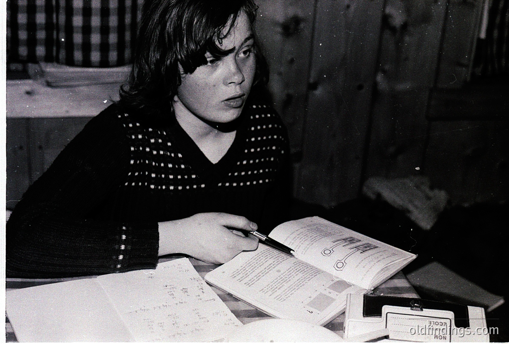 Vintage black-and-white photo of a woman in a patterned sweater studying a passport and handwritten notes, likely at a desk. Visible stamps and a "NON" visa rejection mark suggest travel documentation. Mid-20th century European setting.