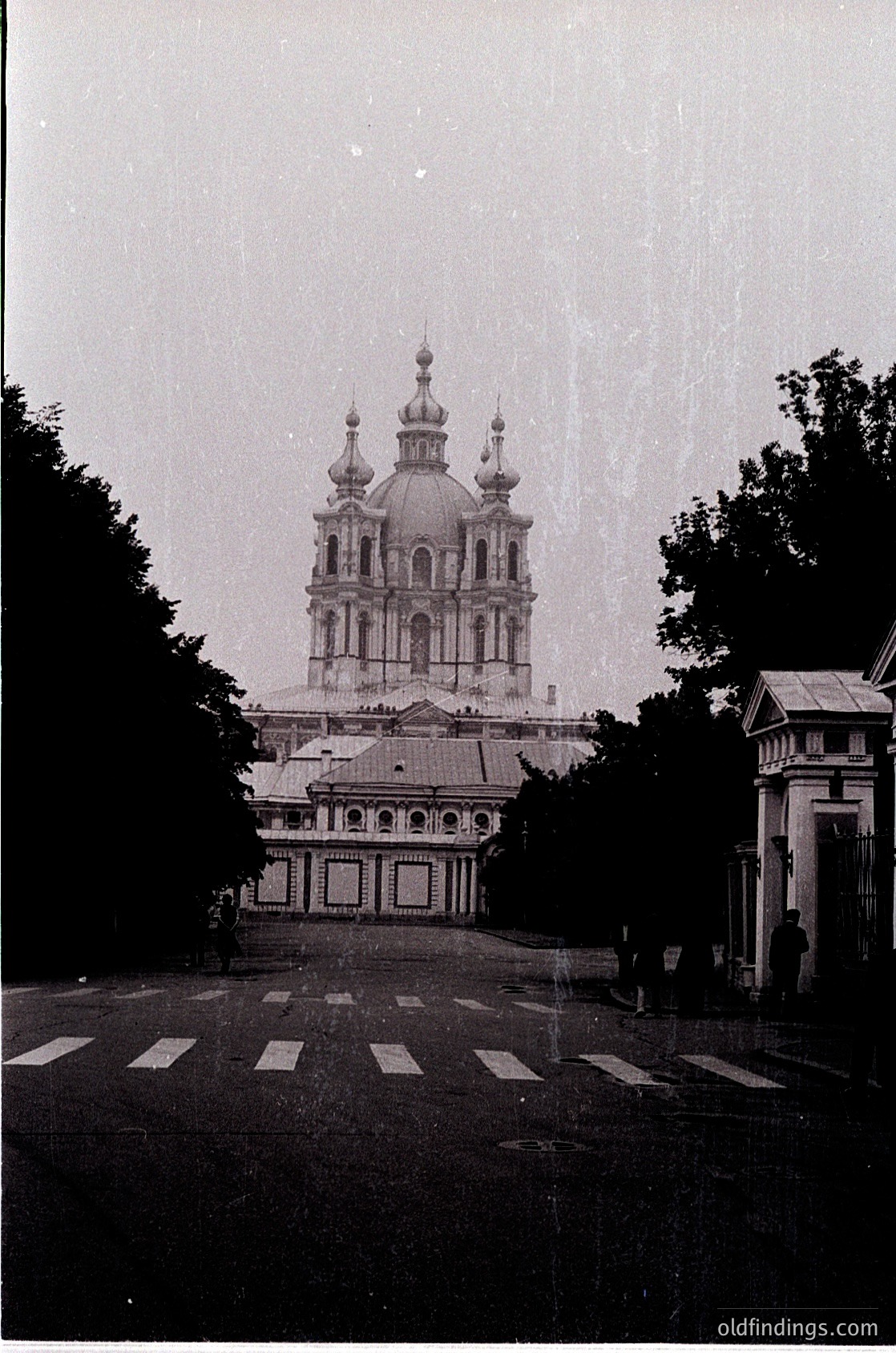 Baroque-style Orthodox church with twin domes and golden crosses, framed by trees and a crosswalk. Likely 19th–early 20th century Eastern European architecture.