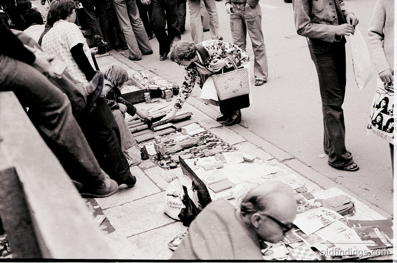 Street market scene featuring vendors selling fresh fish on pavement tables, likely in a European coastal city. Mid-20th century attire (1950s–1960s) and gutted fish suggest a traditional open-air market. Crowd examines wares, indicating active commerce.