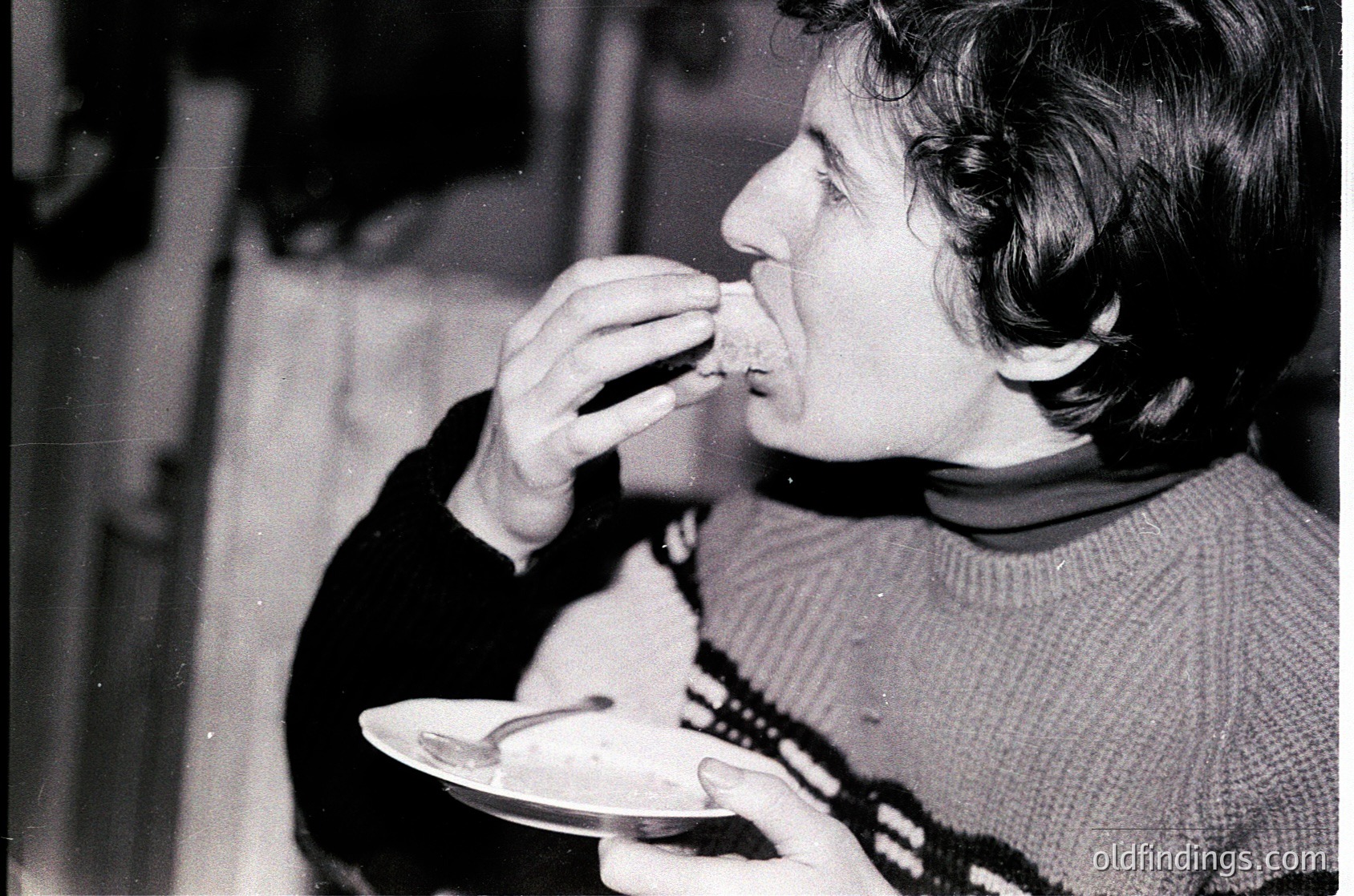 Black-and-white candid shot of an individual eating at a casual indoor setting, likely mid-20th century. Person wears a patterned sweater and holds a spoon, focusing on food. Vintage grain and lighting suggest a home or small gathering. Ideal for historical or nostalgic research.